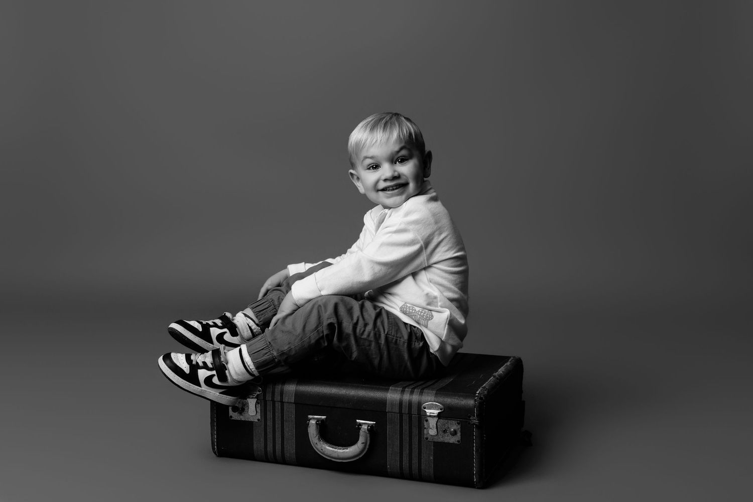 Professional photo series featuring a child interacting with vintage suitcases in studio lighting.