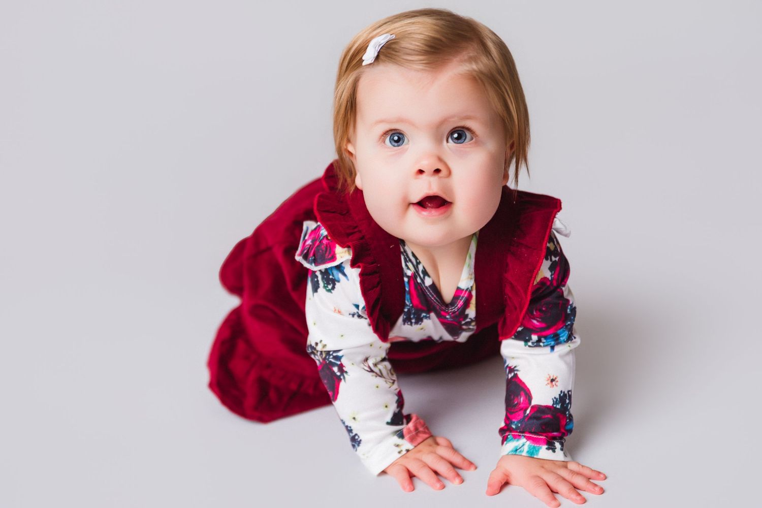 Baby in red velvet dress exploring studio space.