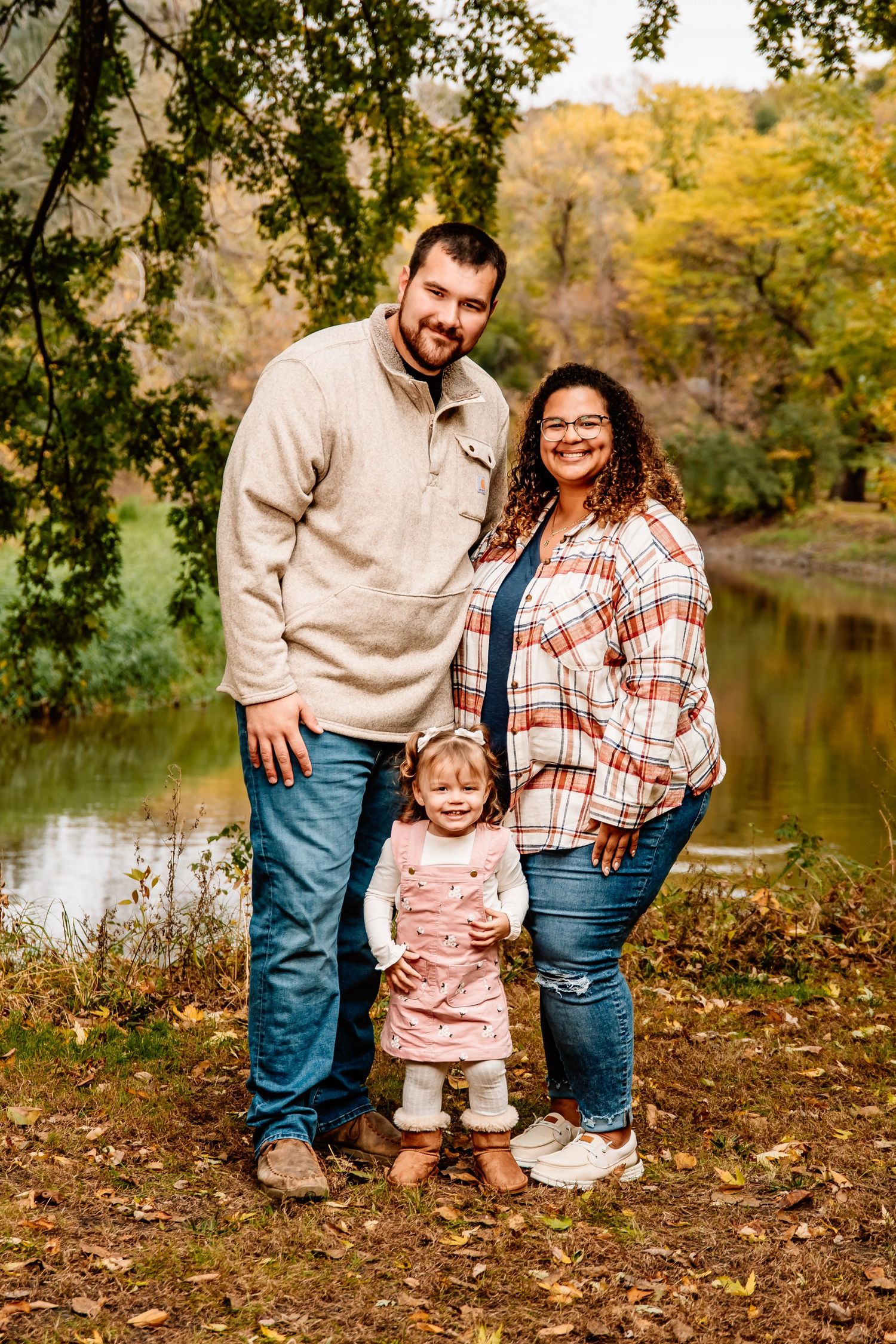 A family poses together on fallen autumn leaves near a tranquil pond during a fall photoshoot.