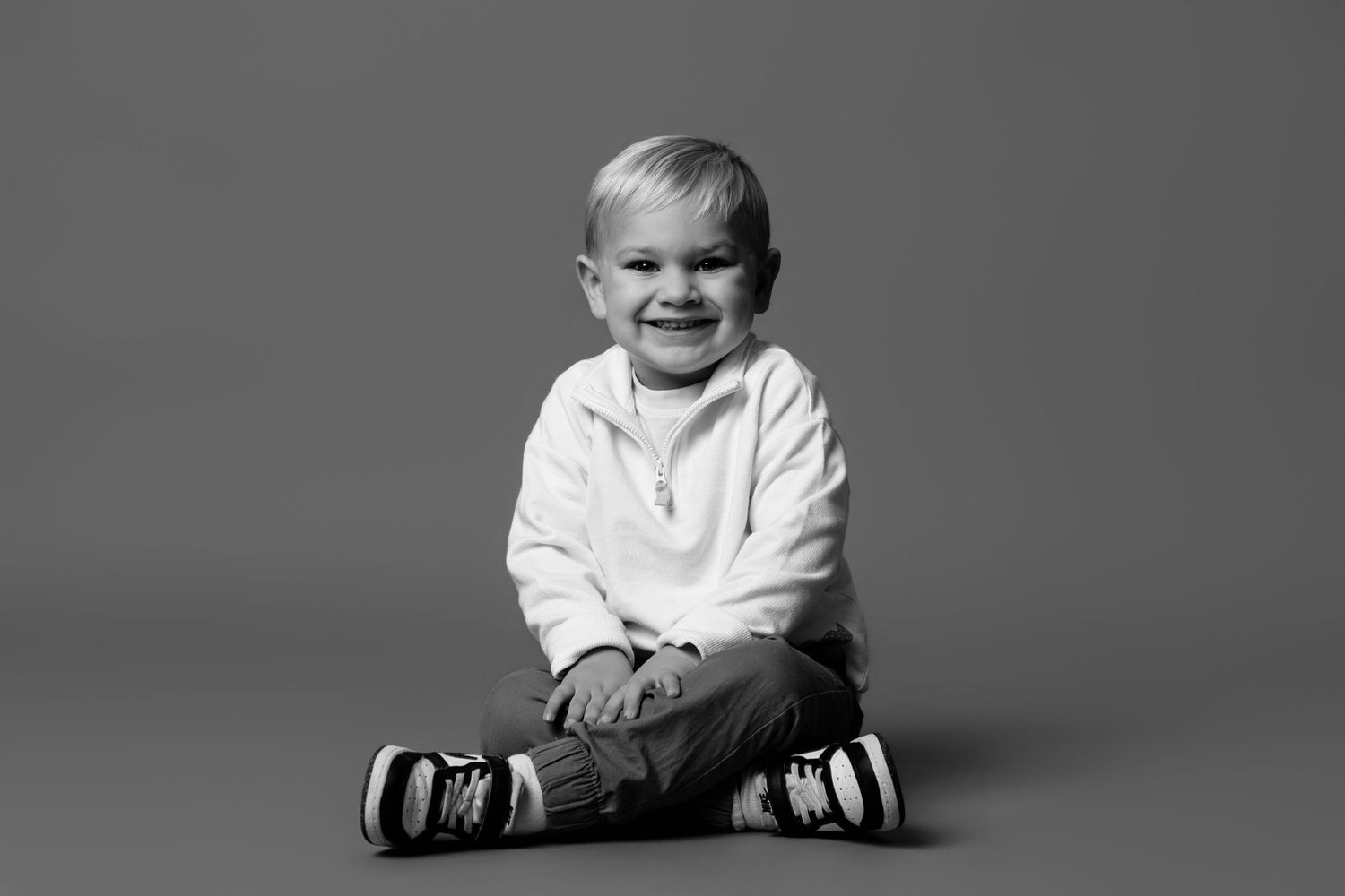 A black and white portrait series shows a child sitting in various playful poses against a simple studio backdrop.