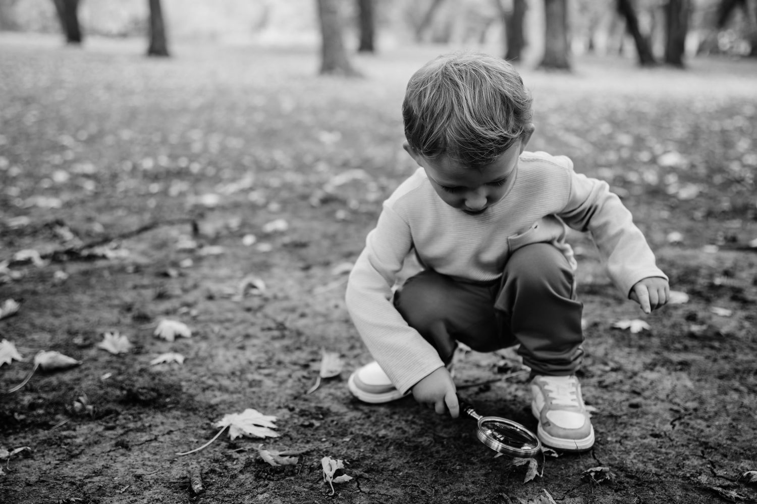 Child explores fallen autumn leaves on the ground in black and white photography.