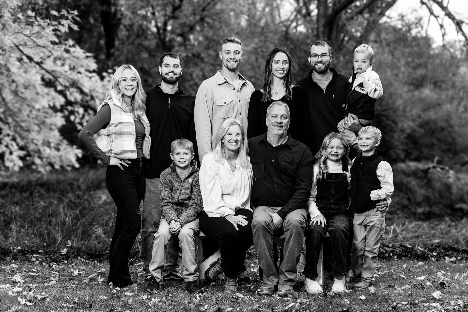 A black and white photo series showing a family sitting together outdoors during a fall portrait session.