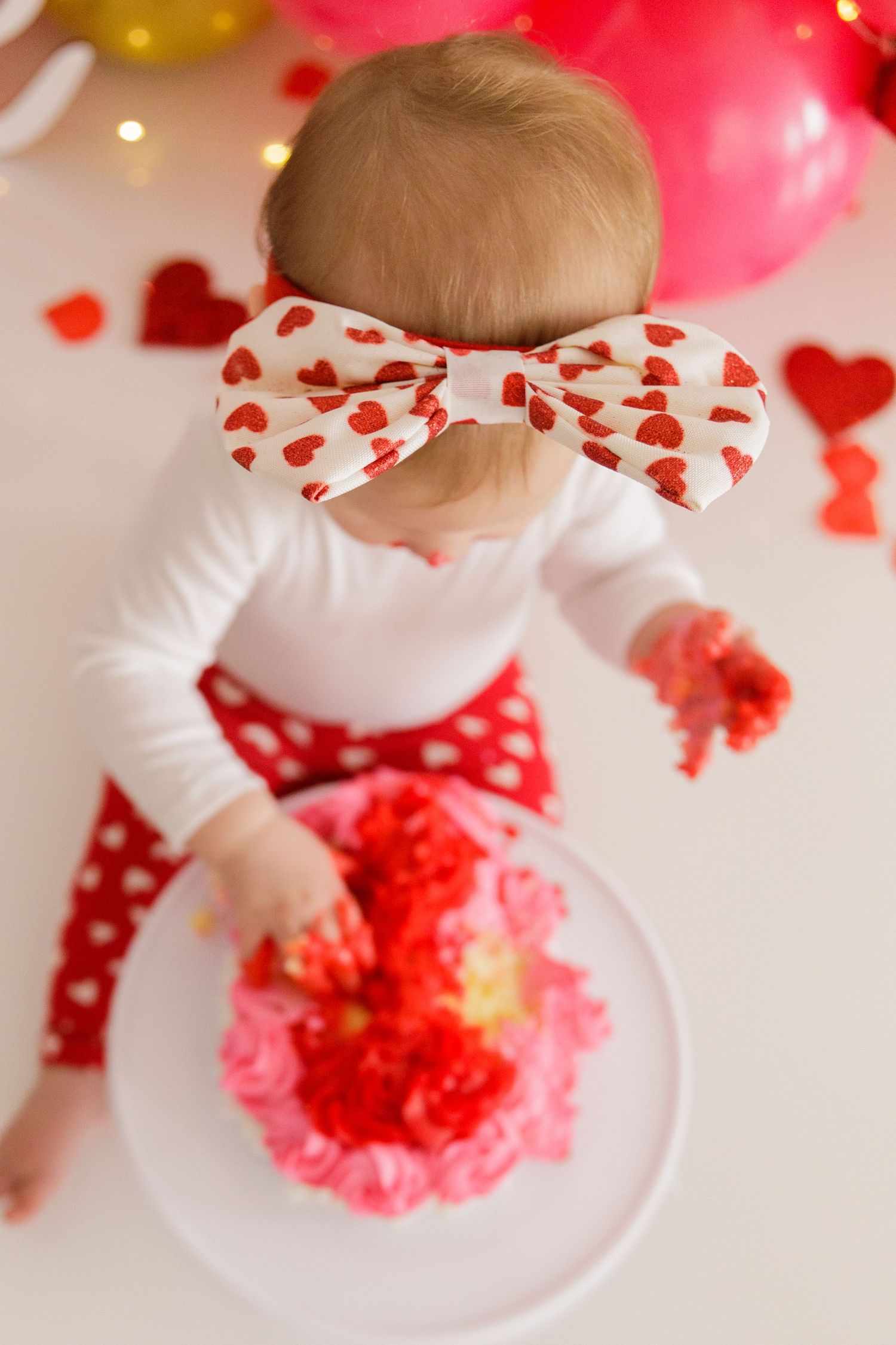 Close-up shots of a Valentine's Day cake smash session with red and pink decorations.