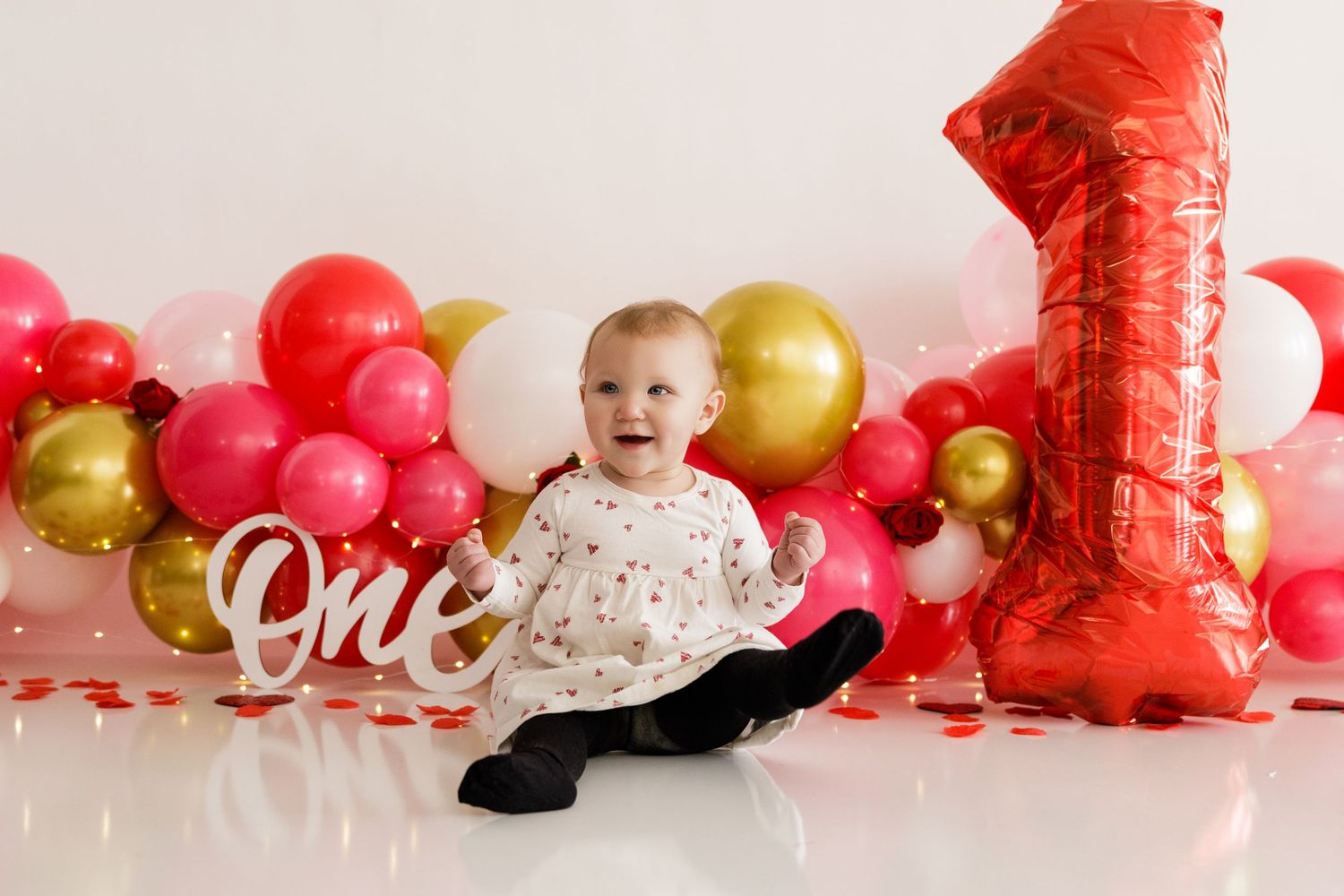 A baby's first birthday cake smash photo session with red and gold balloons and decorations.
