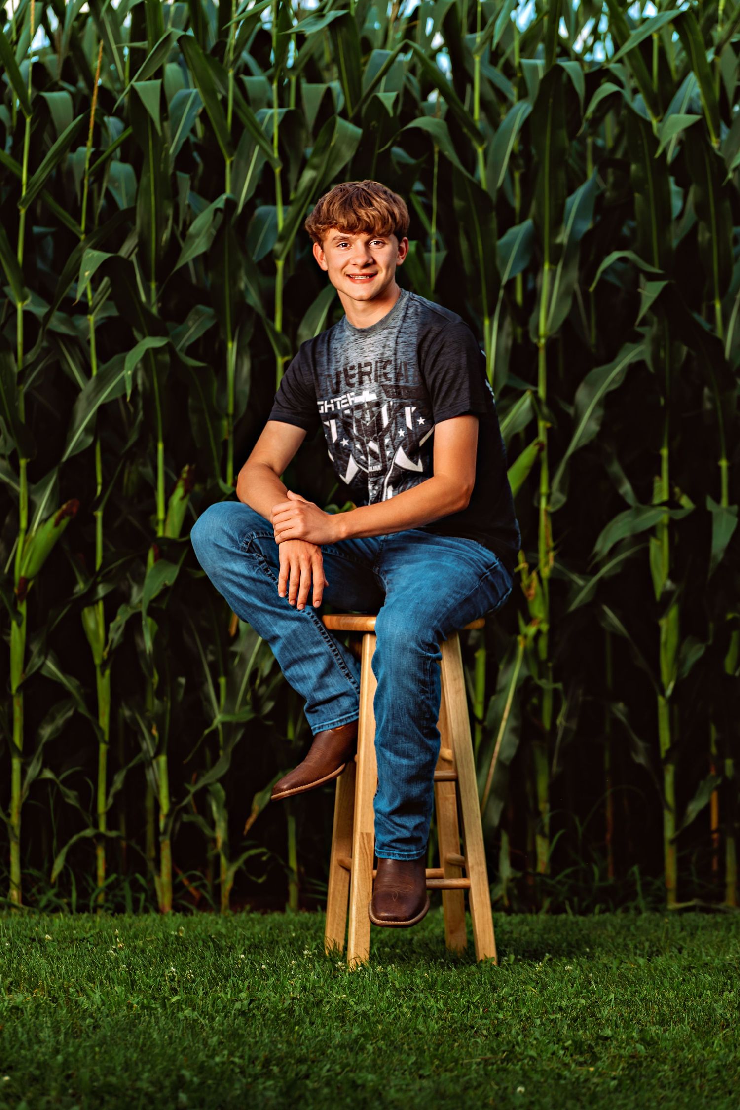 Portrait of someone sitting on a wooden stool against tall green corn stalks at sunset.