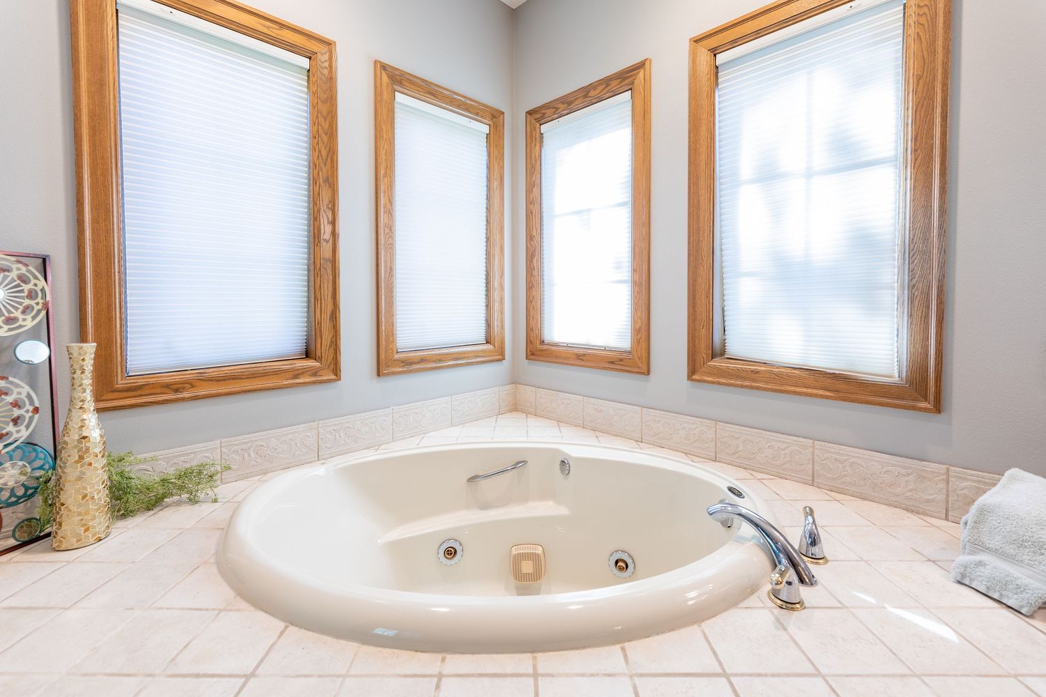 Luxurious corner jetted bathtub surrounded by tile and three wood-framed windows in a bright bathroom.