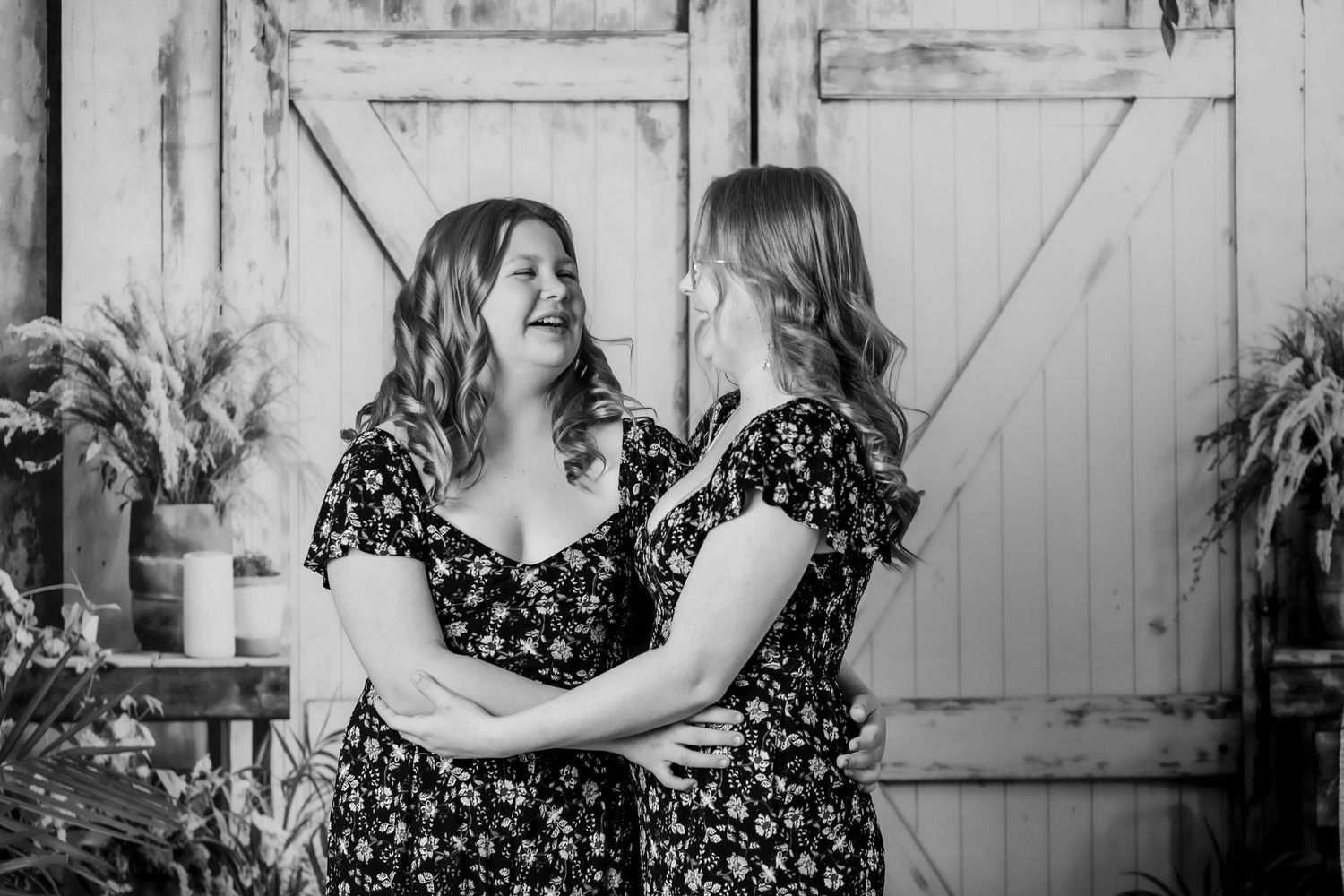 Two women in matching floral dresses smiling and embracing in black and white portrait photo.