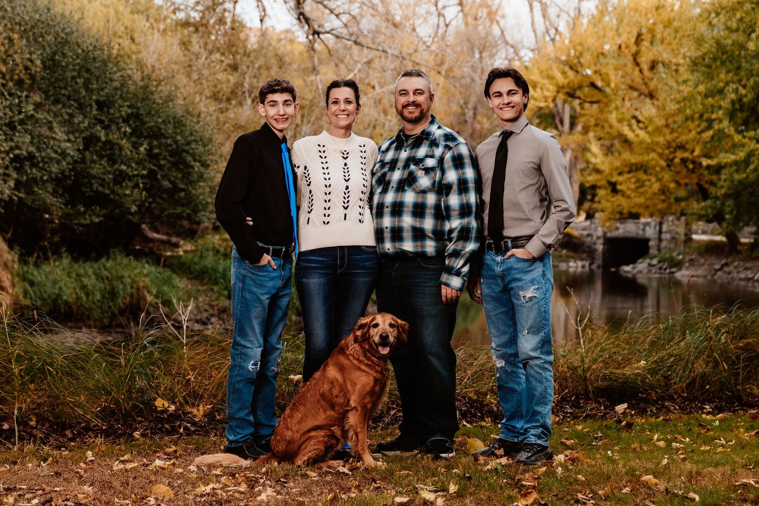 A group poses together in a scenic autumn setting with golden leaves and trees in the background.