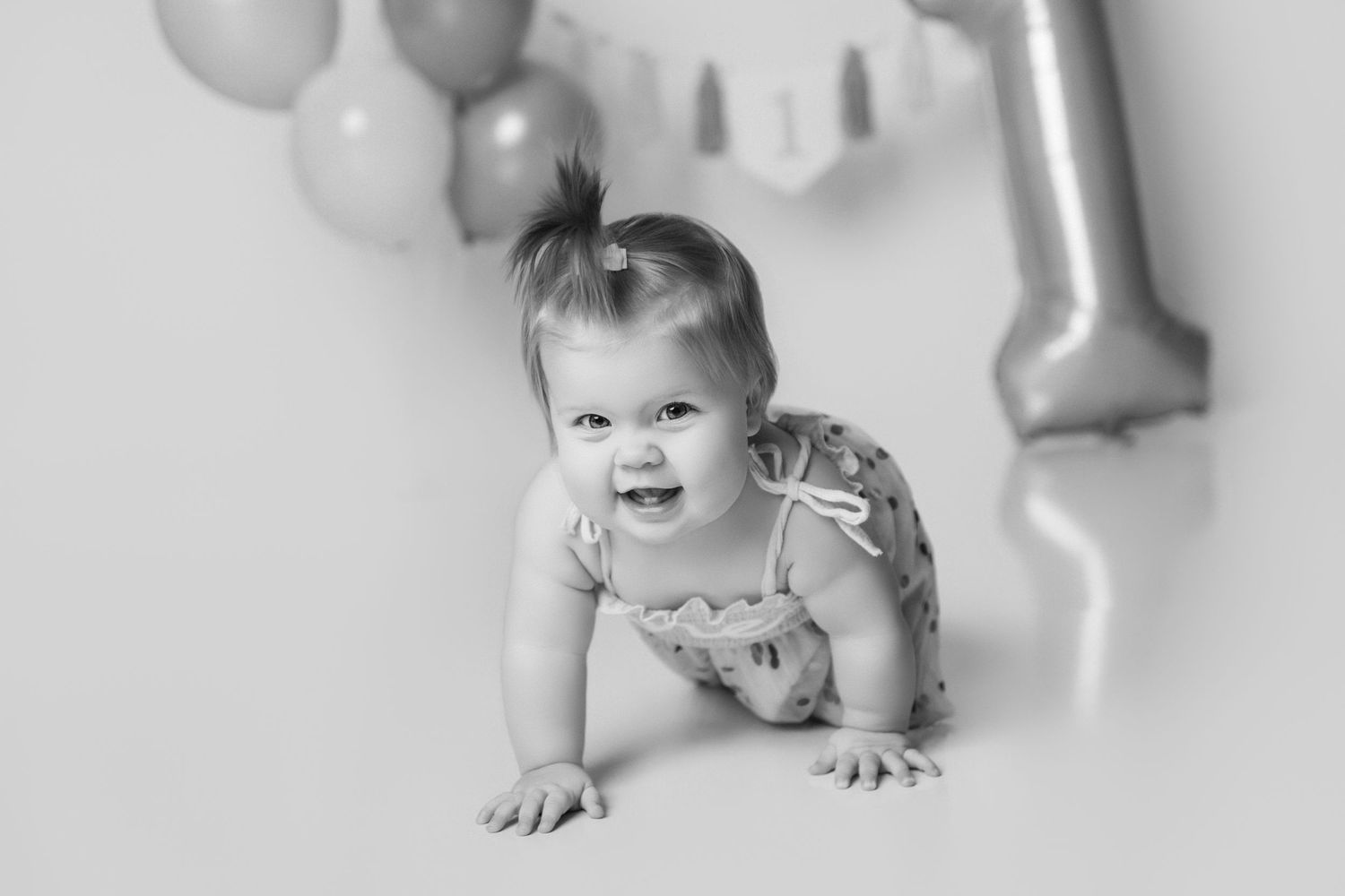 Baby crawling on white floor with gray and pink balloon decorations.