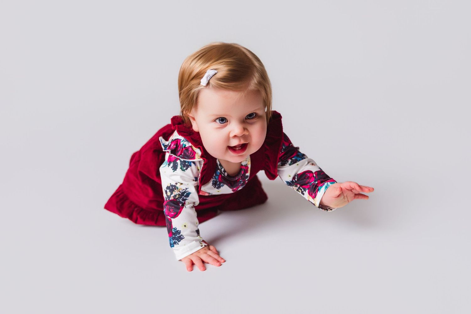 Baby in red outfit crawling on white background during photo session.