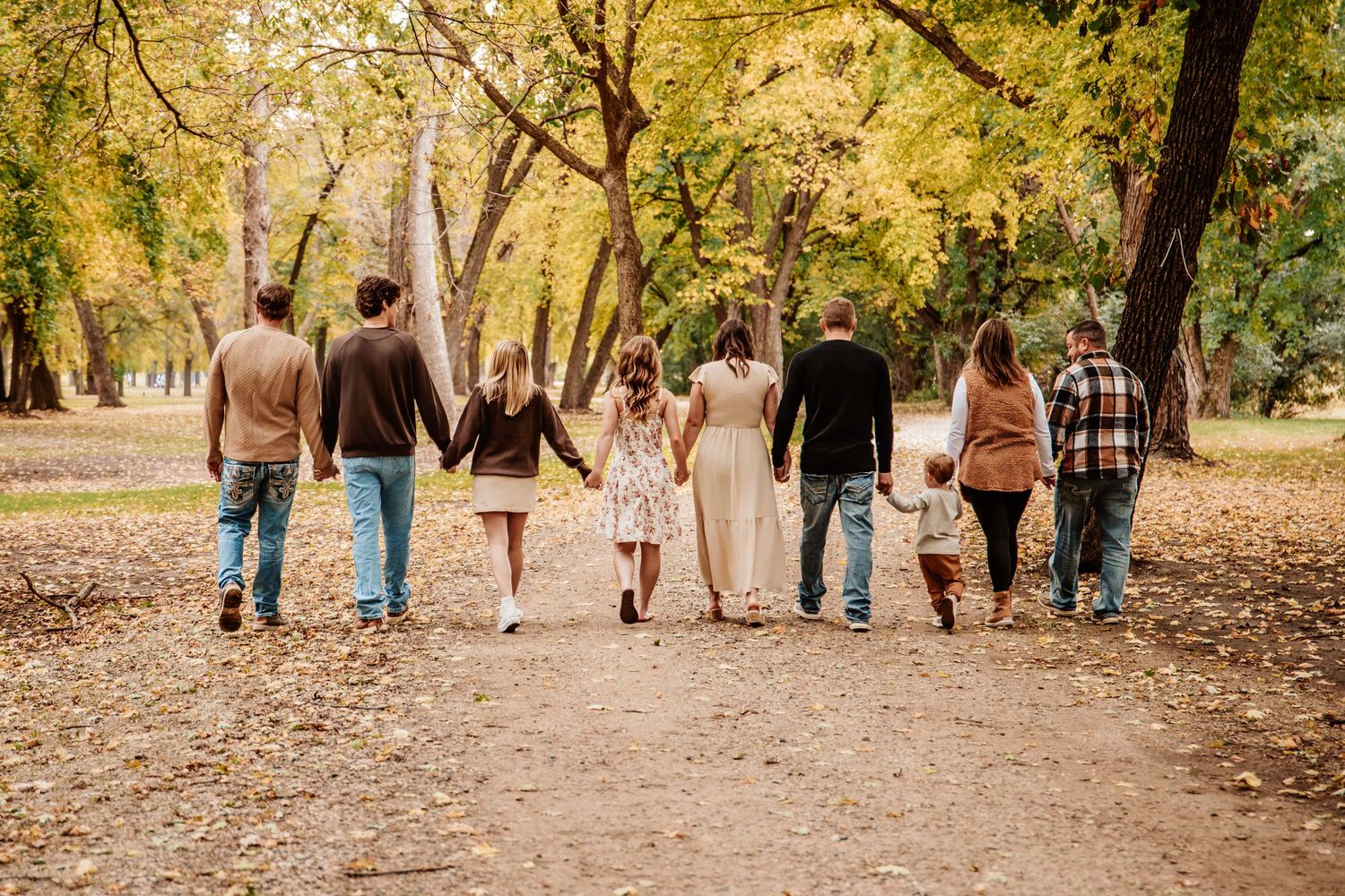 Group walking together on a leaf-covered path through golden autumn trees.