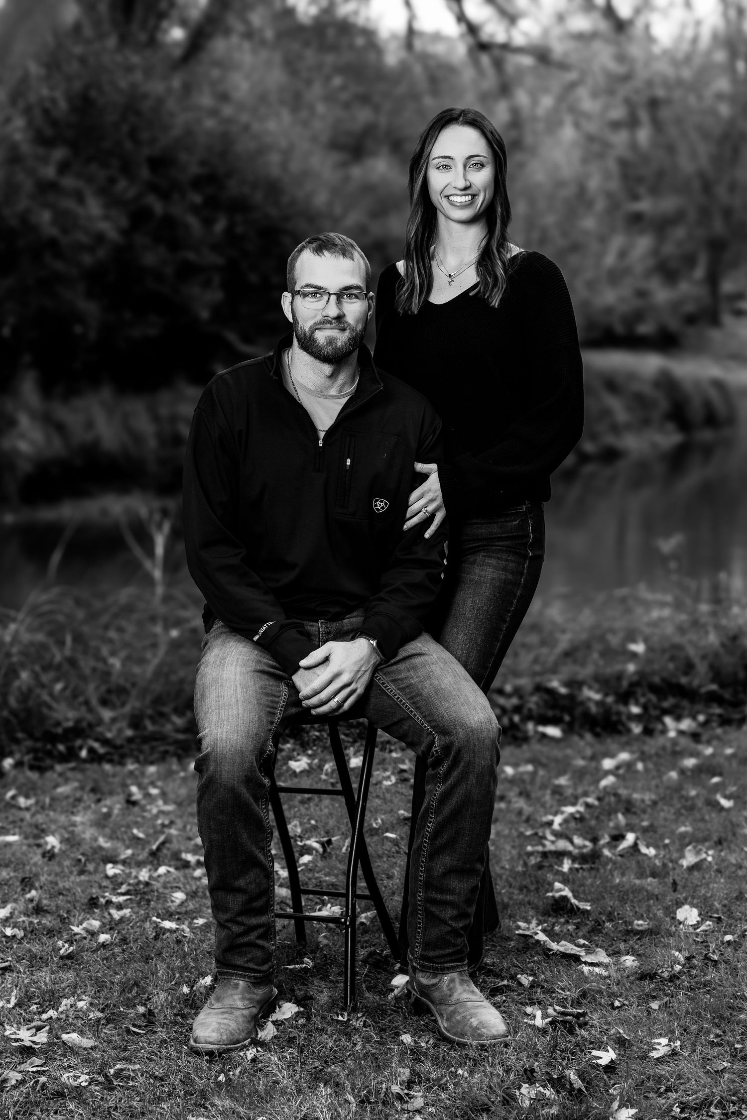 Couple sitting together outdoors on fallen leaves during an autumn photo session.