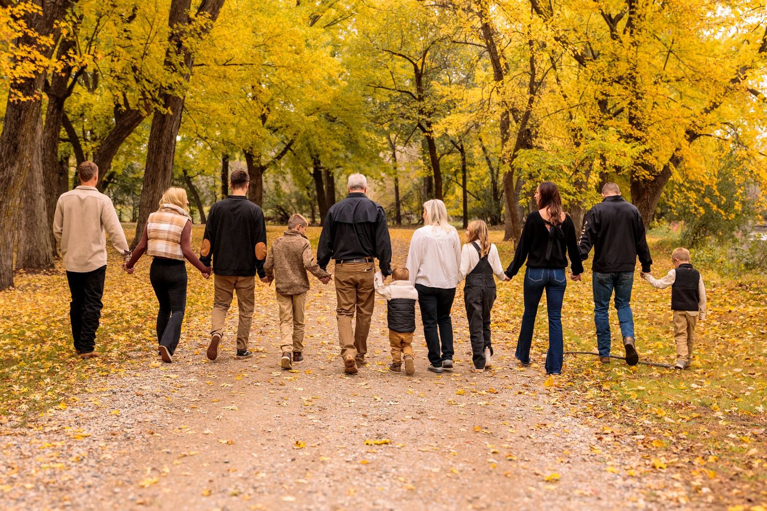 Large group walking together on path lined with golden fall foliage.