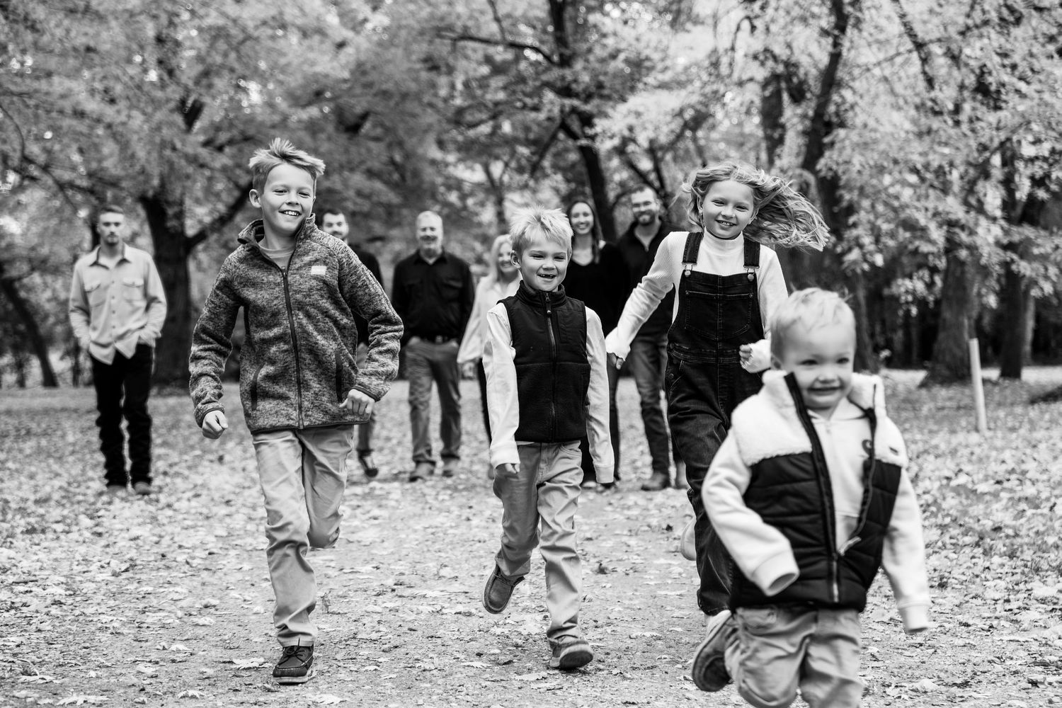 Black and white photo of people walking together through a leaf-covered park path.