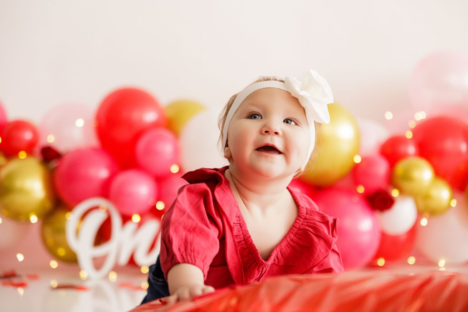 Festive balloon arch with pink, red and gold balloons against white background.