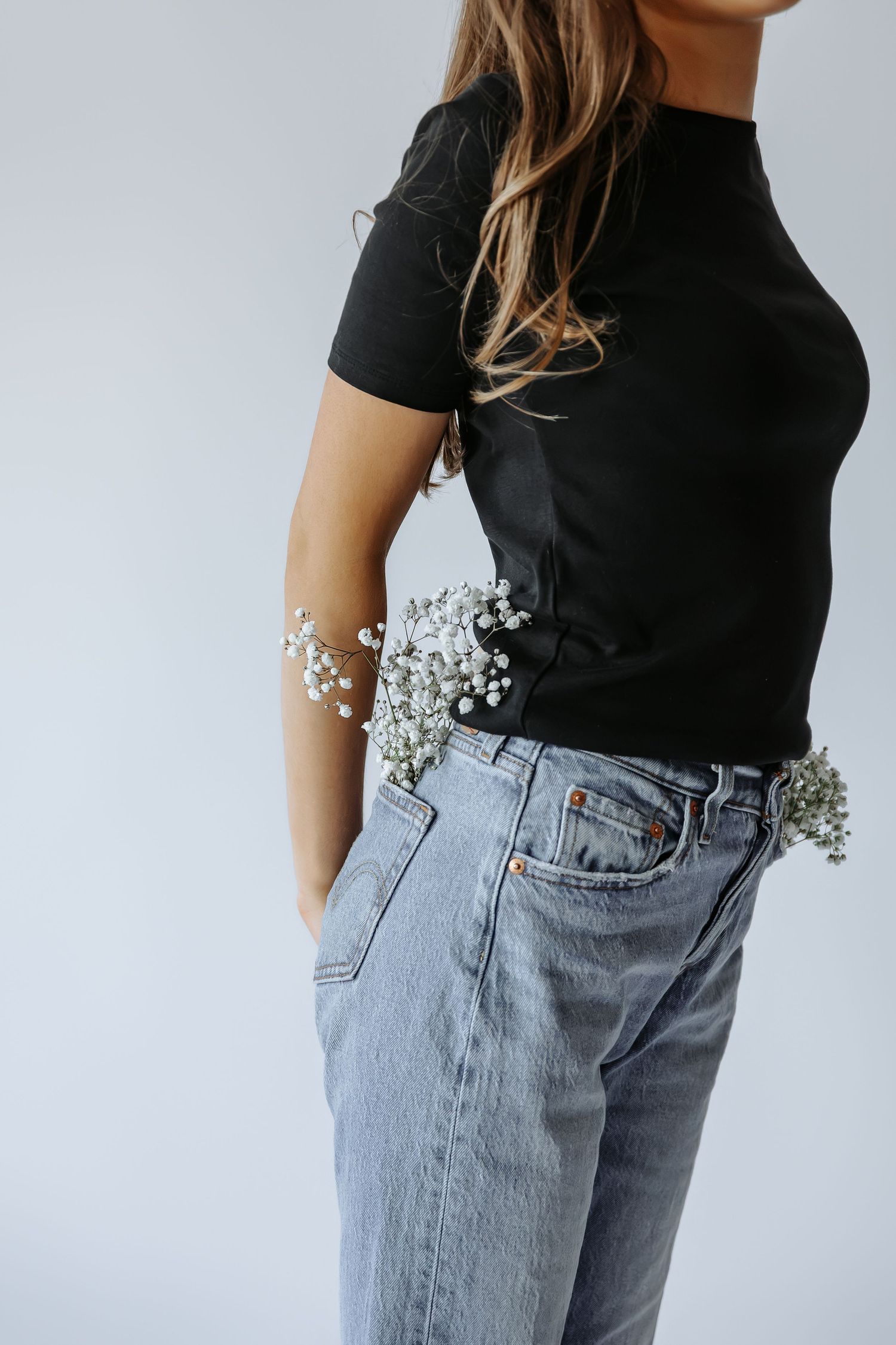 Close-up of woman in black tee and light blue jeans with baby's breath flowers tucked in waistband.