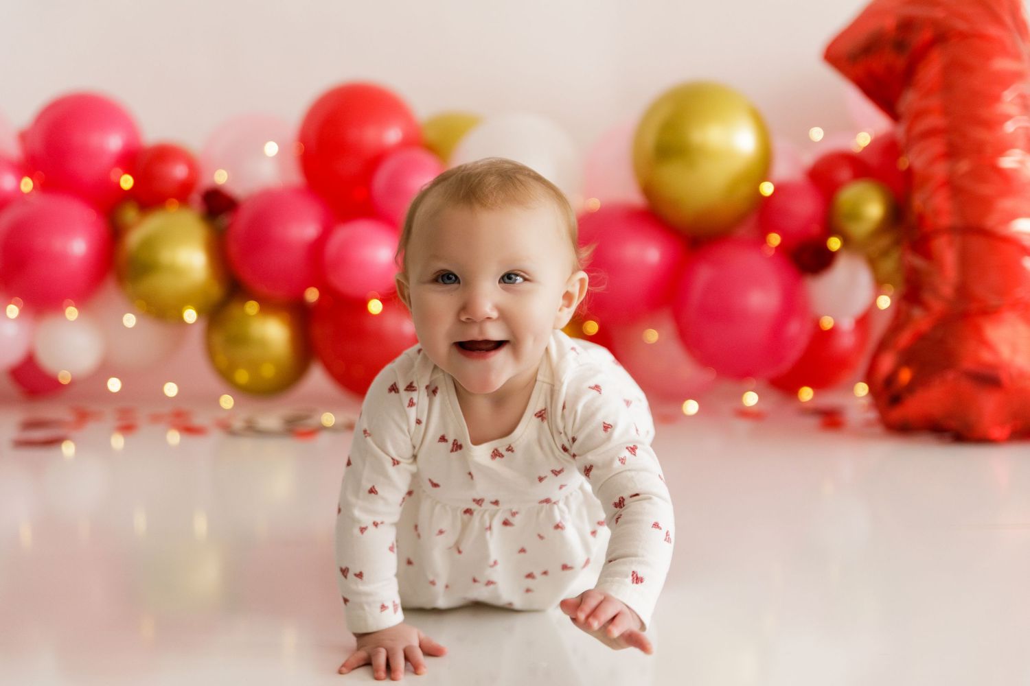 Festive pink and gold balloon backdrop with red decorative elements for a celebration.