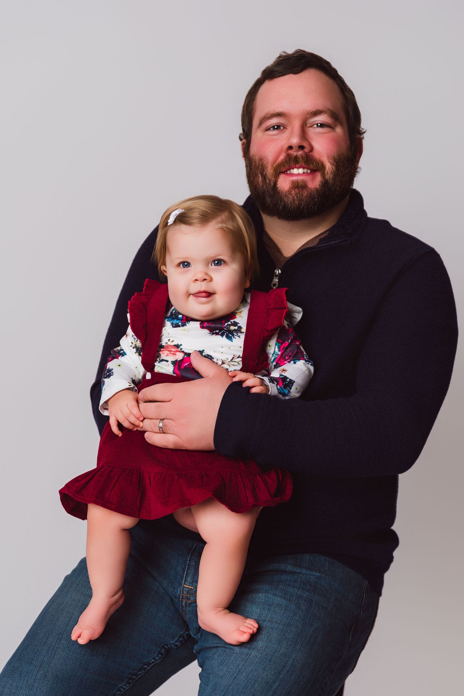 A series of studio portraits showing a baby in a burgundy dress with floral details being held.