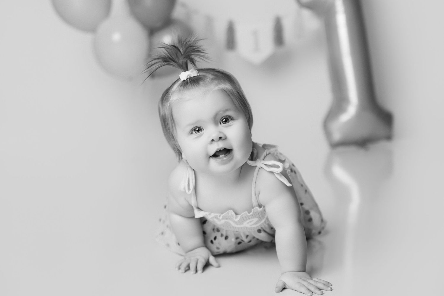 Black and white close-up of baby crawling with birthday decorations in background.