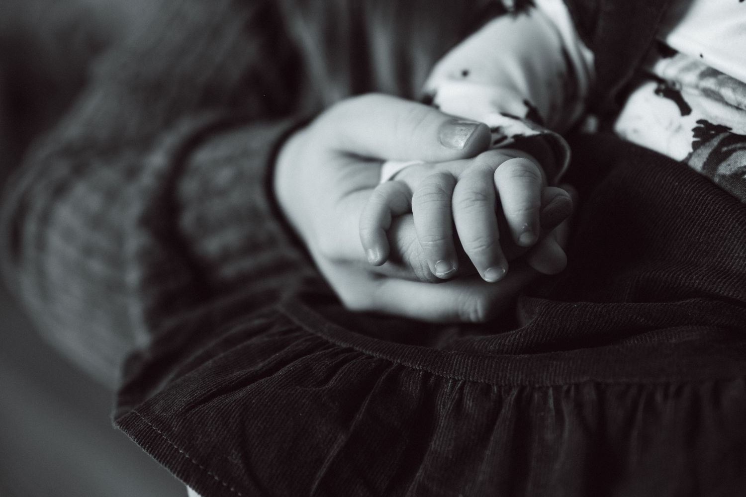 Artistic black and white detail of small hands resting on dark fabric.