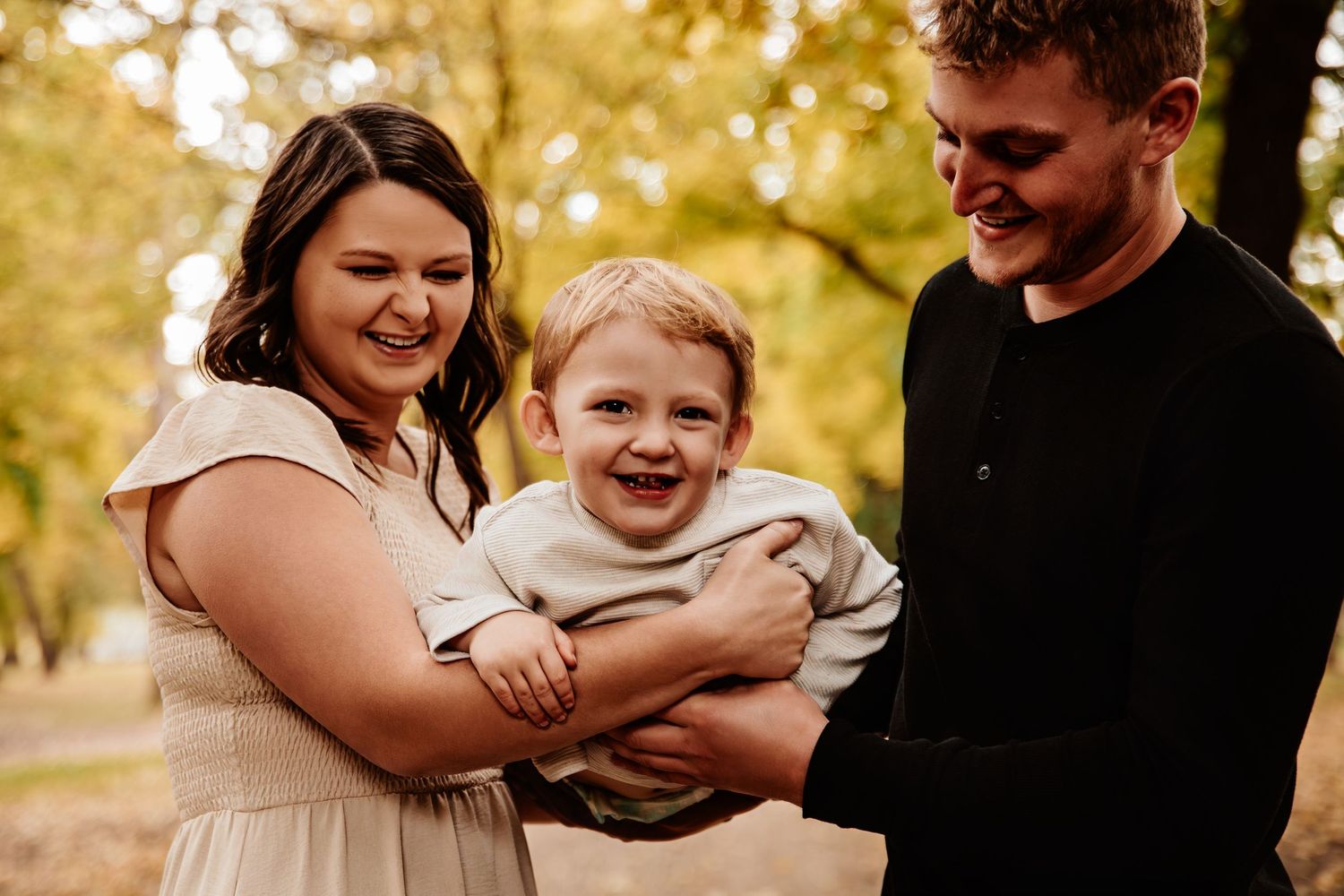 A happy family shares a joyful moment together outdoors during fall, with their laughing child in the middle.