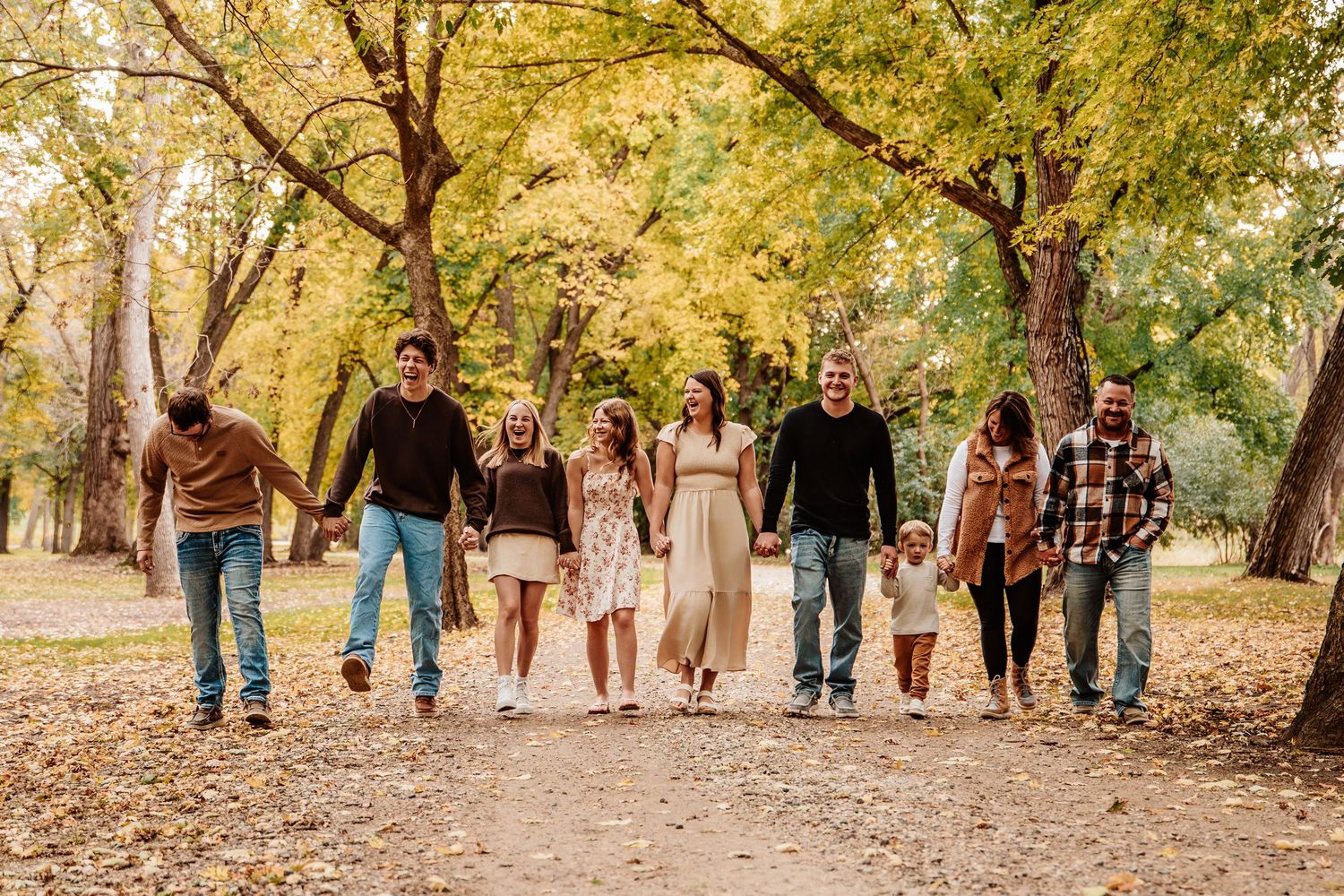 Group walking together on a tree-lined path covered in autumn leaves.