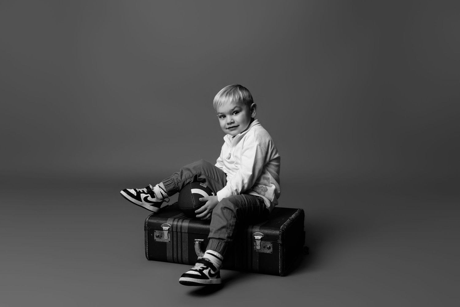 Child playing with cardboard box in minimalist black and white studio setting.