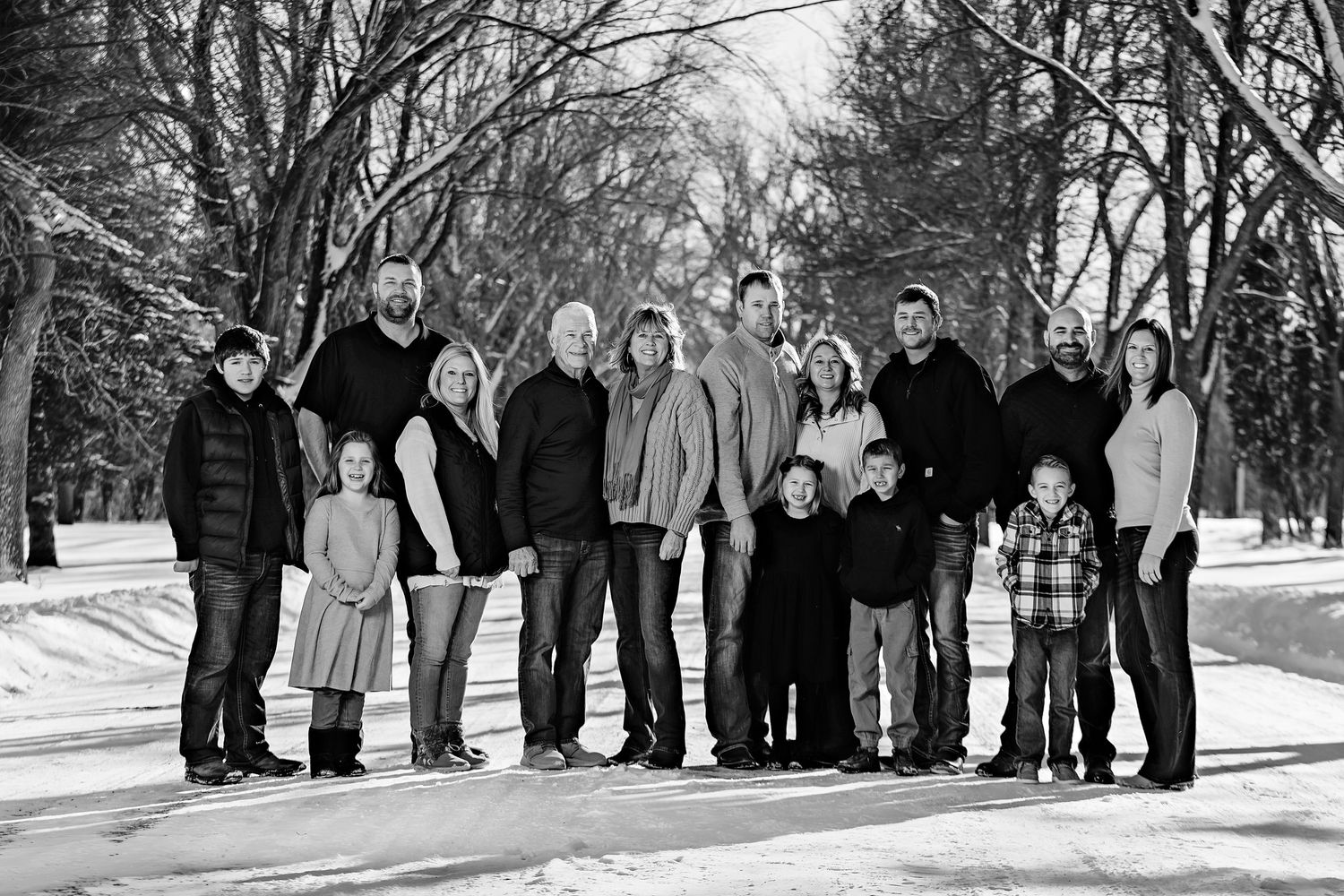 Multiple people stand together in winter coats on a snow-covered walkway with trees in the background.