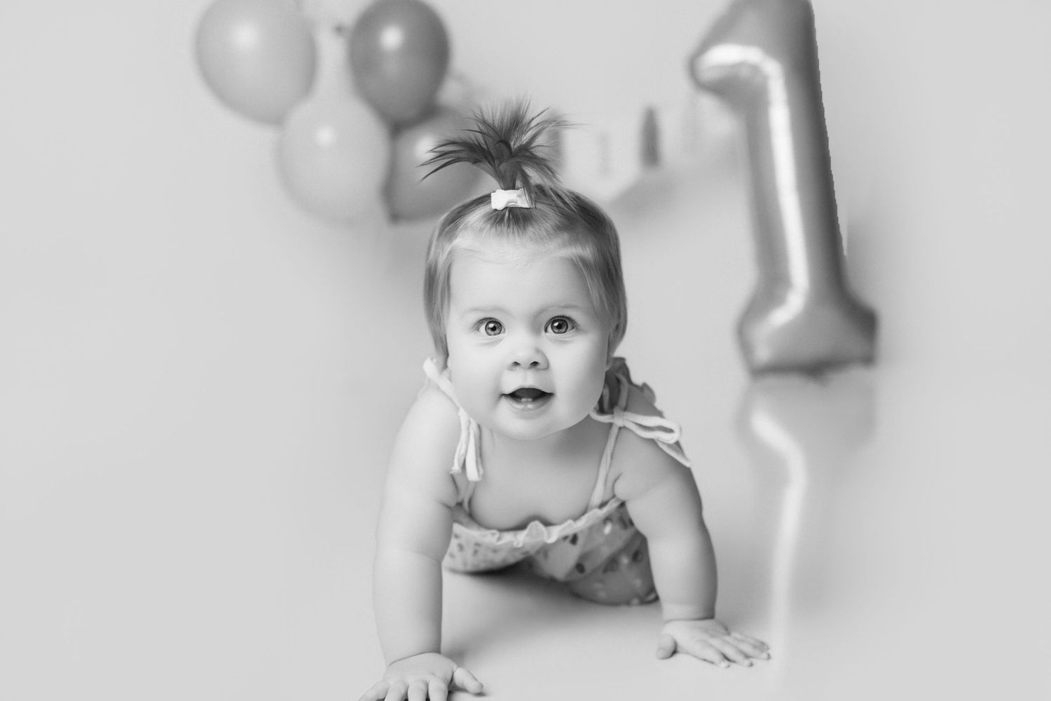 Baby surrounded by silver and white balloons during celebration photoshoot.