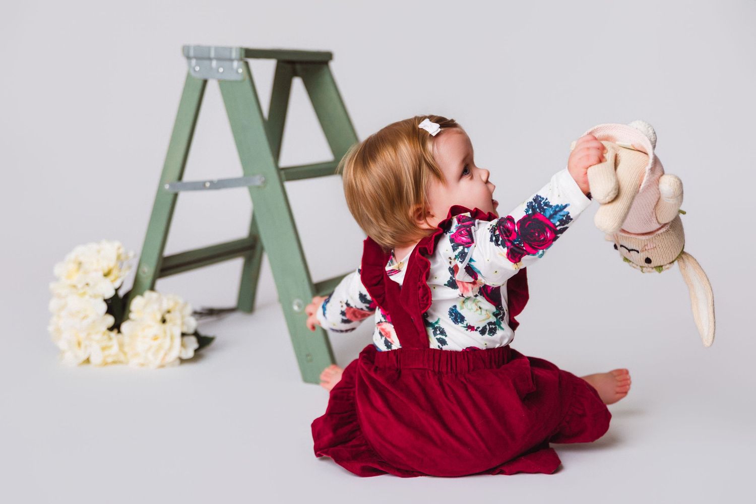 Studio shots of a baby playing with popcorn near a green ladder prop.