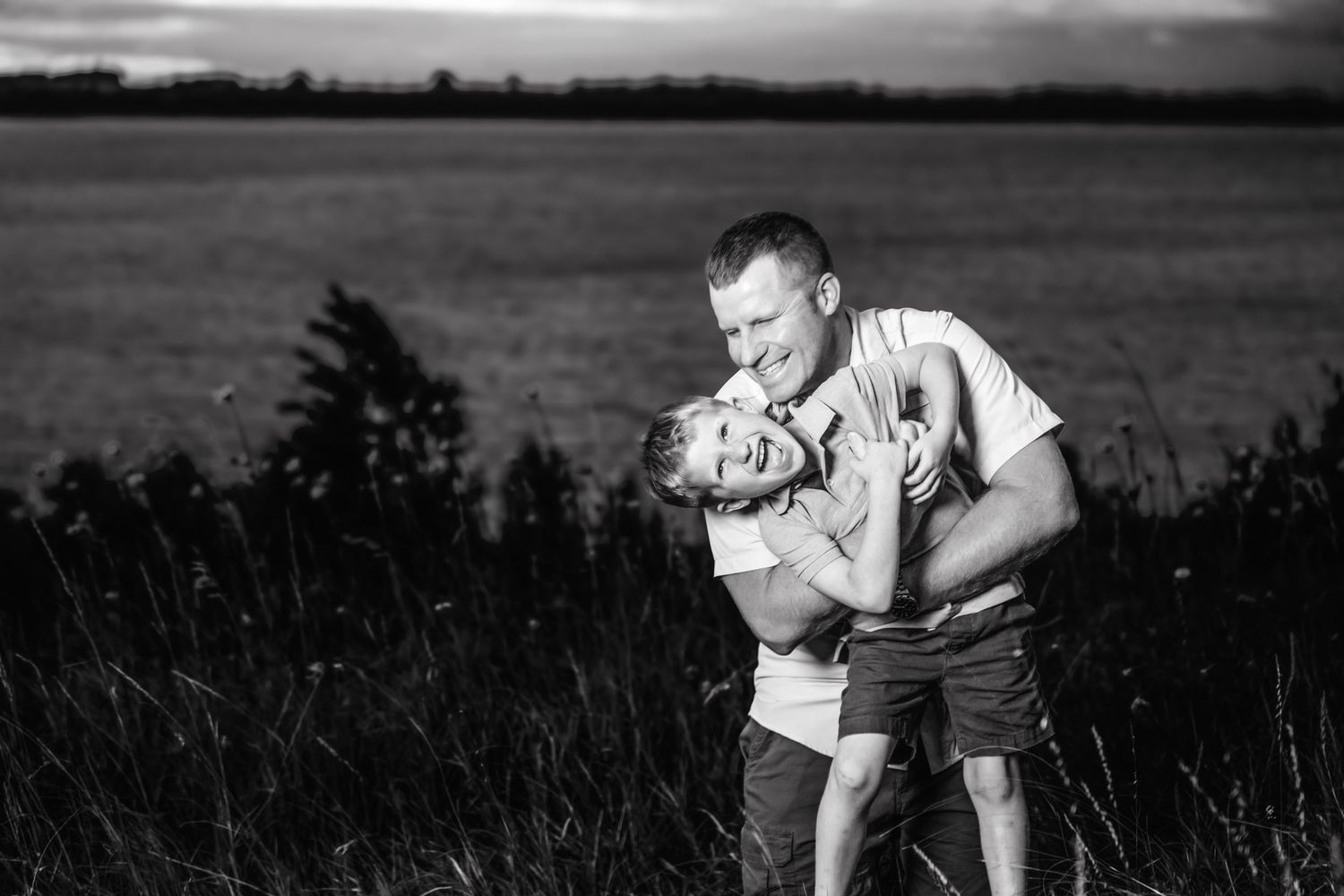 Black and white portrait of two people embracing in a field at dusk.