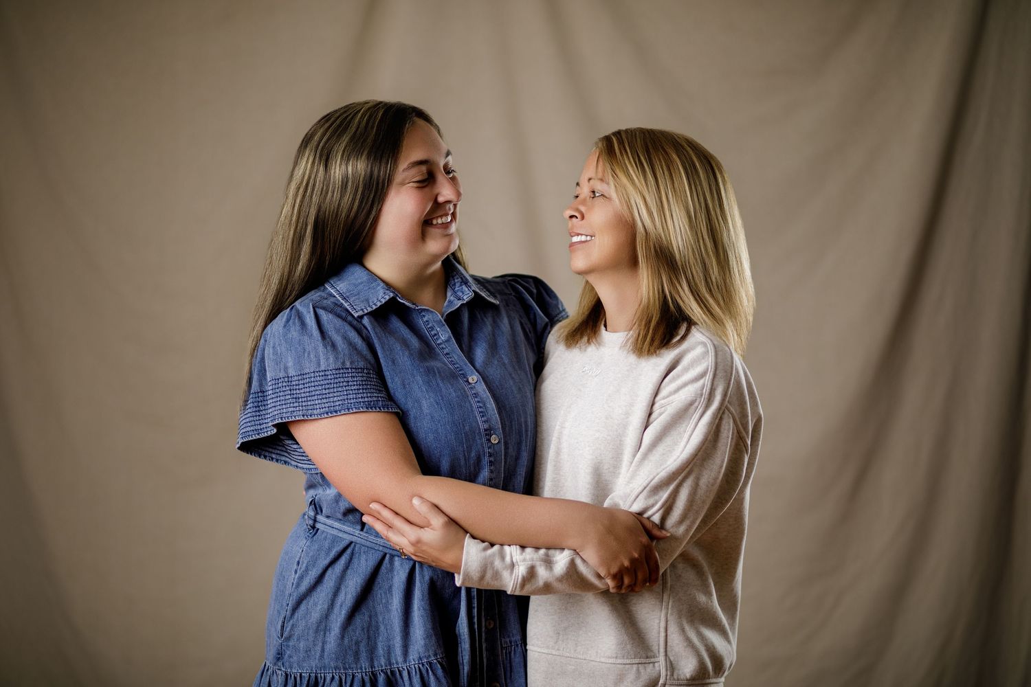 Two smiling women embracing and looking at each other in a warm studio portrait photo.
