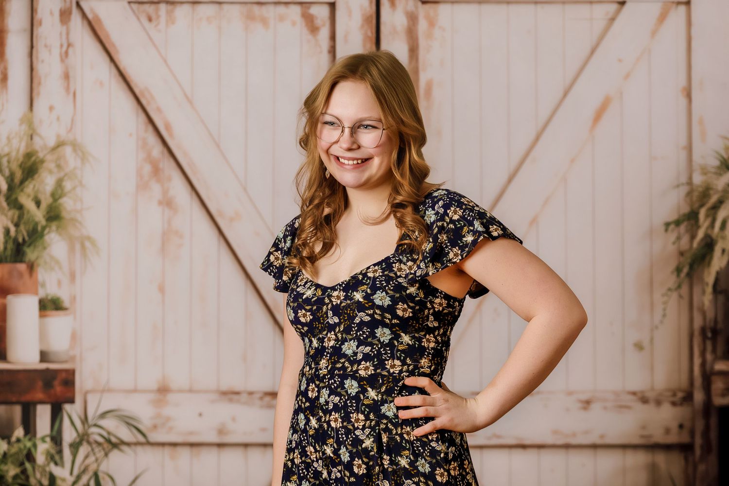 Young woman in floral dress smiling confidently in front of a rustic wooden barn door backdrop.