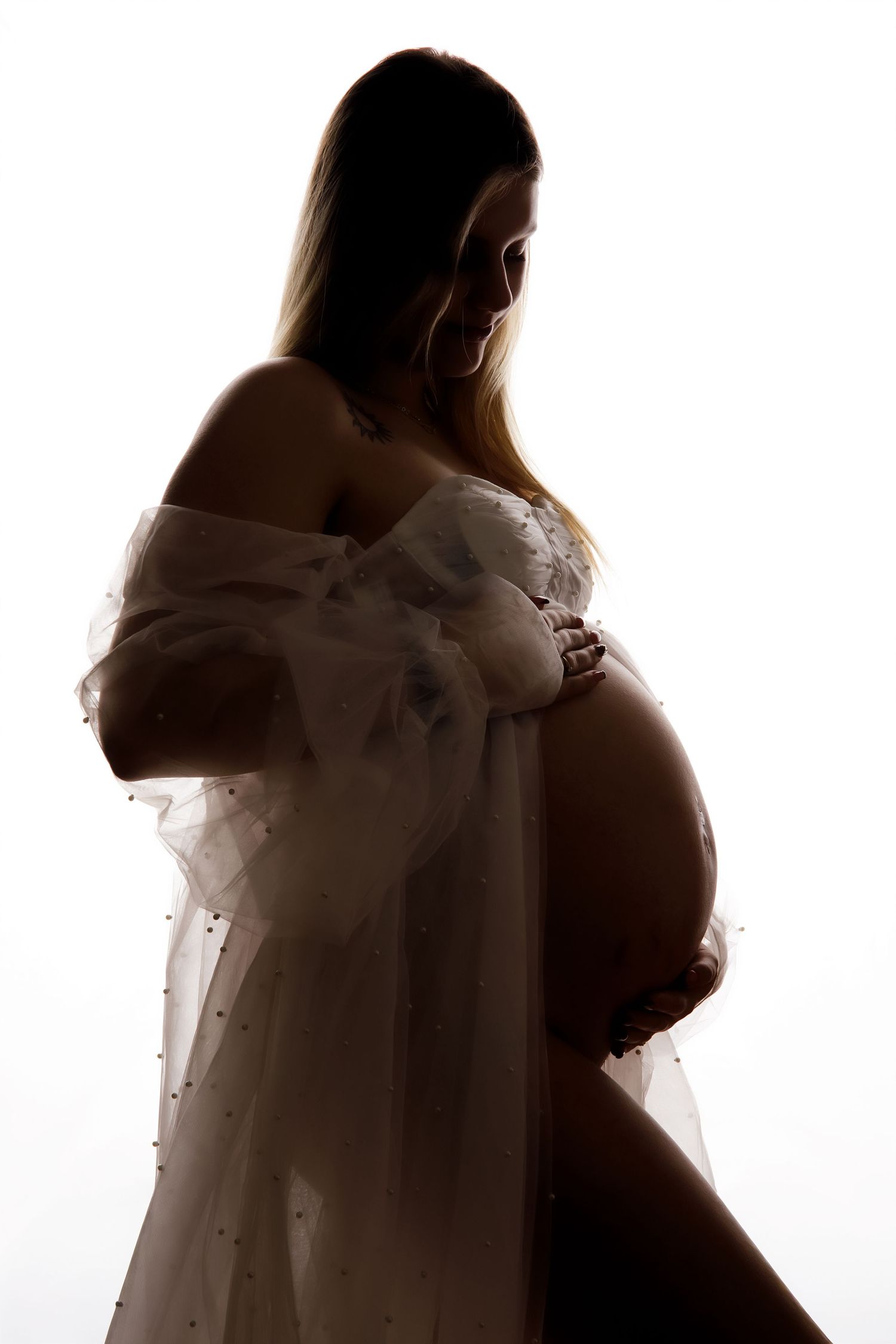 Silhouetted maternity portraits showing a pregnant woman in a flowing white dress against a bright background.
