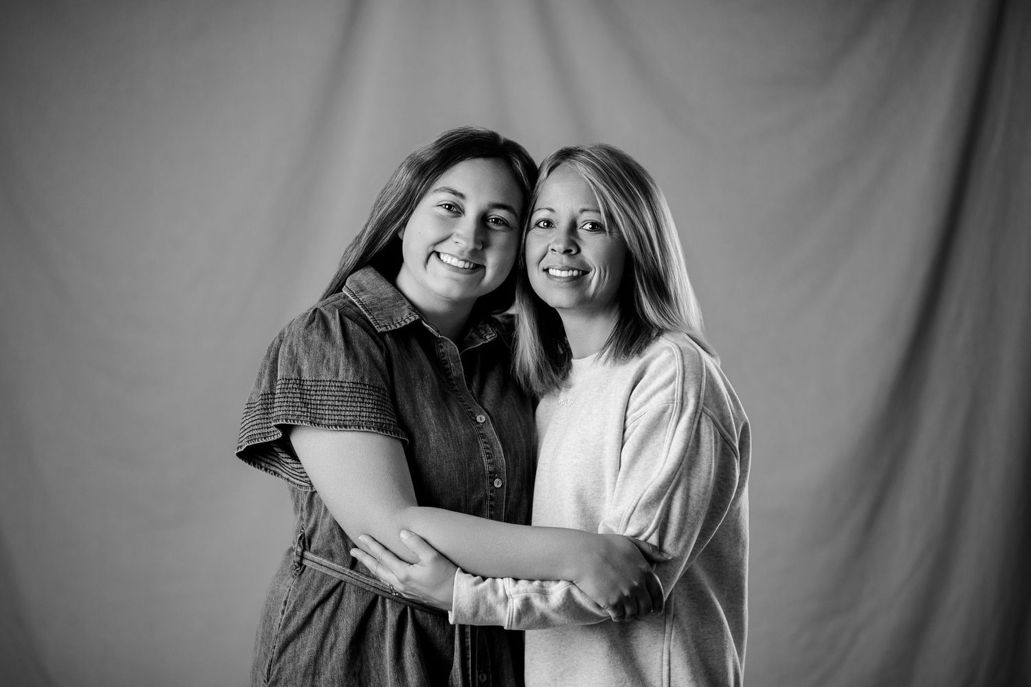 Two smiling women embracing in a black and white studio portrait photo.