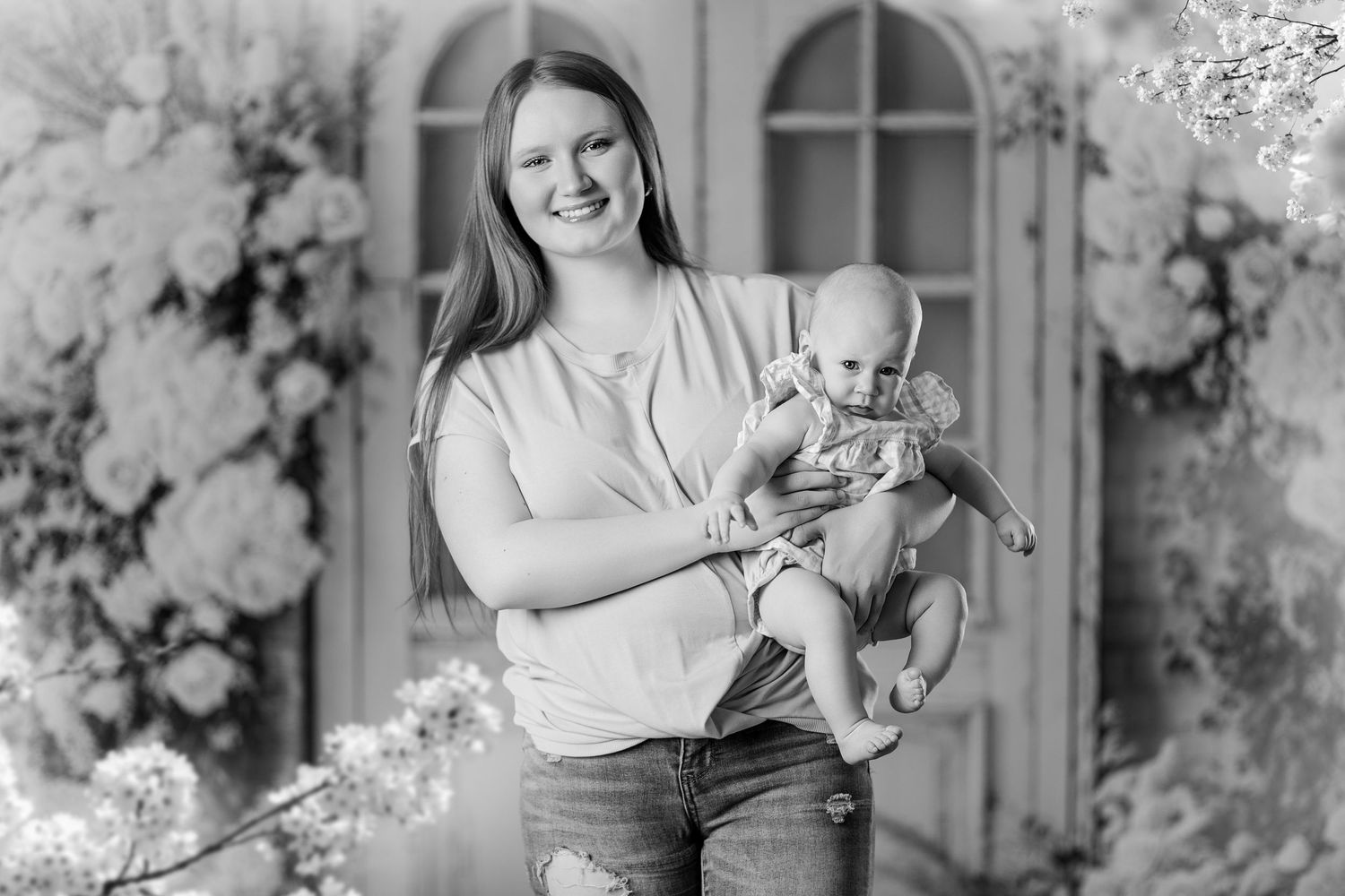 Woman smiling and holding a baby in a black and white floral portrait photo.