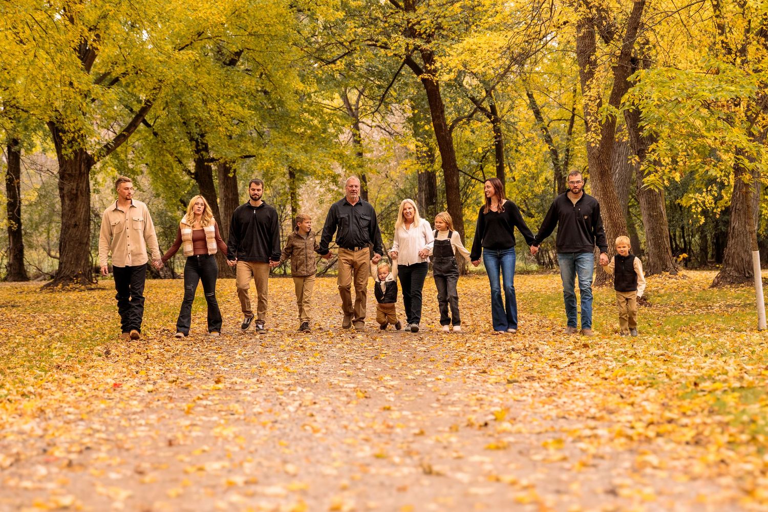 Group of people walking in line through a park filled with yellow autumn leaves.