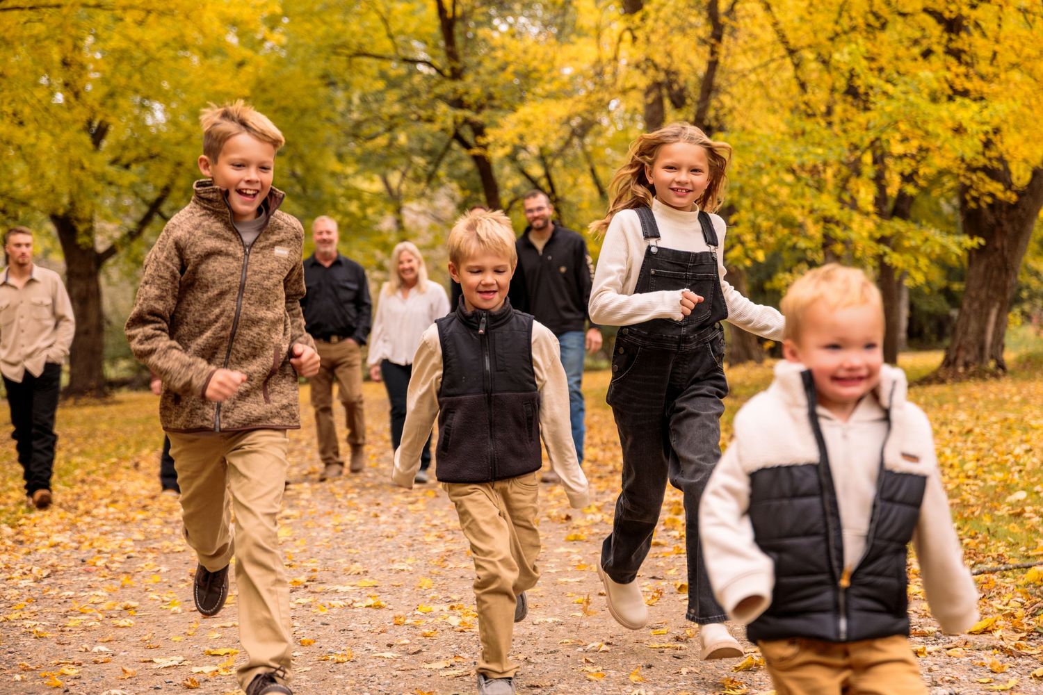 People running and playing together through golden autumn leaves in a park.