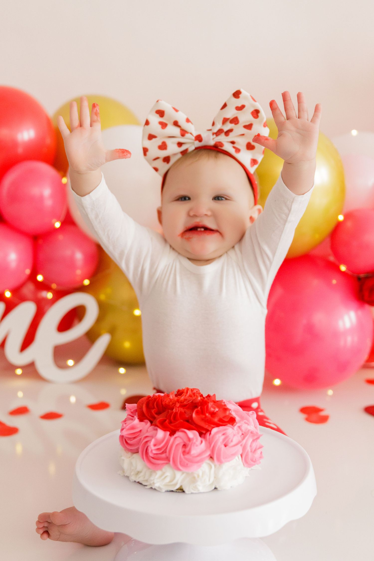 White cake platform decorated with pink rosettes against balloon backdrop.