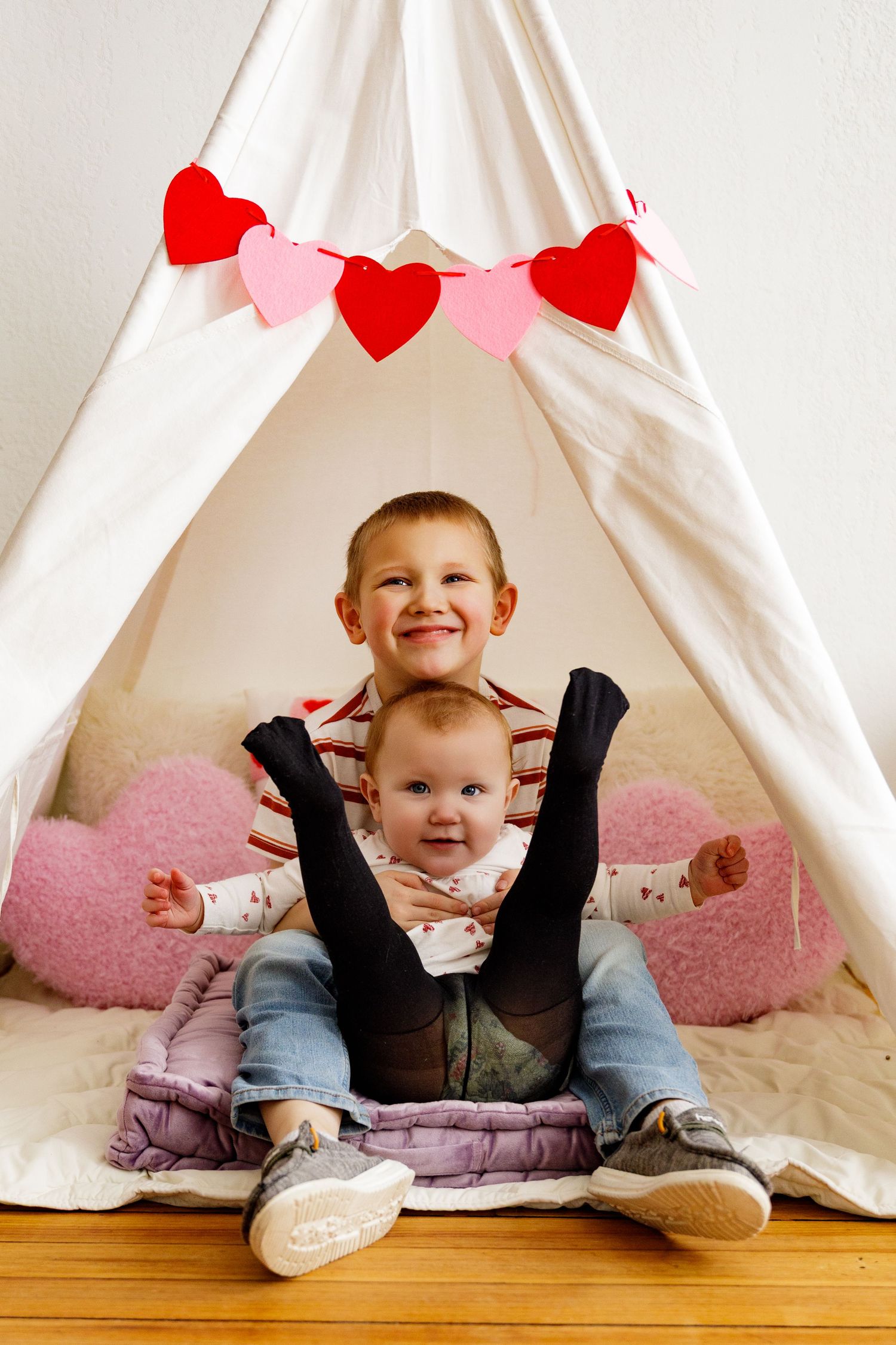 Small figure sitting under white teepee tent decorated with red and pink heart garland.
