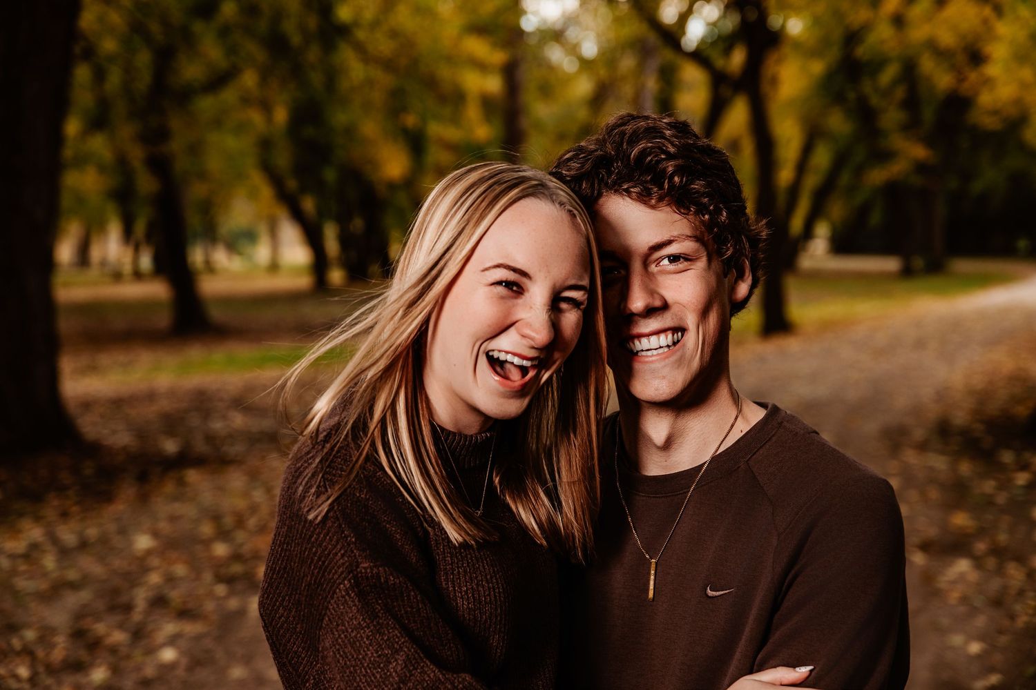 Couple shares intimate moment while laughing together in autumn forest setting.
