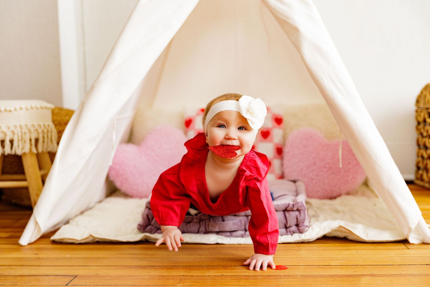 White teepee tent setup on wooden floor with Valentine's day decorations.