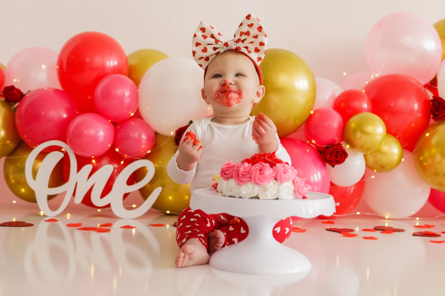 Valentine's Day themed first birthday setup with balloon garland and 'ONE' text decoration.