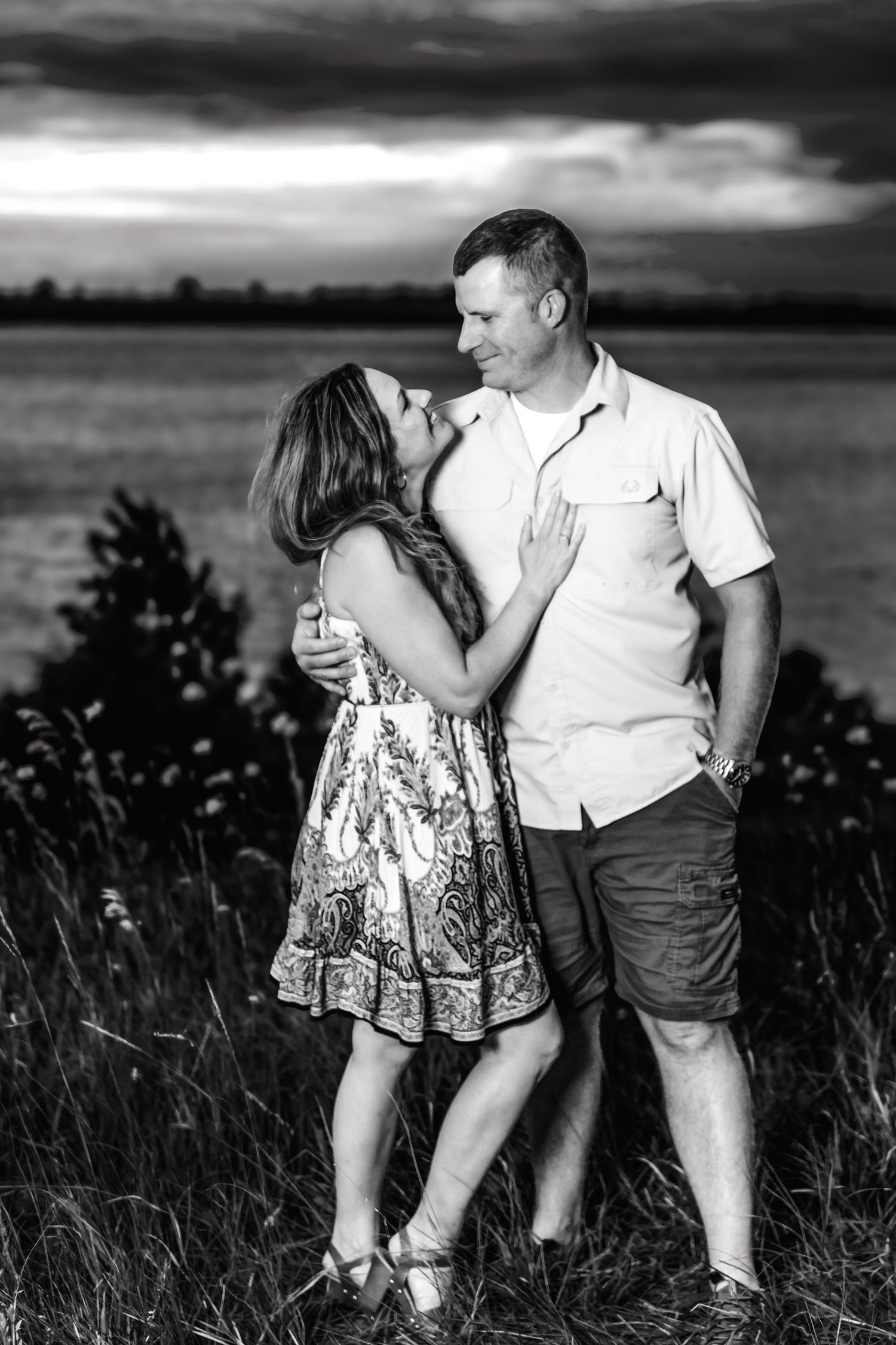 A romantic black and white portrait of a couple in a field at dusk.