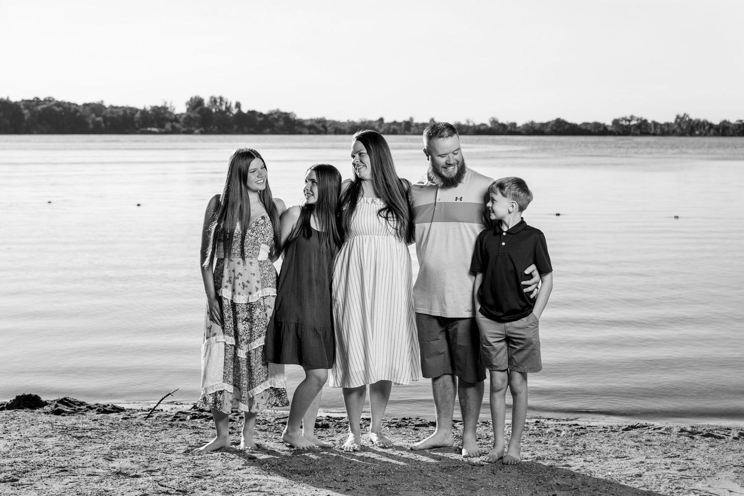 Black and white family portrait of five people standing together by a lake shore.