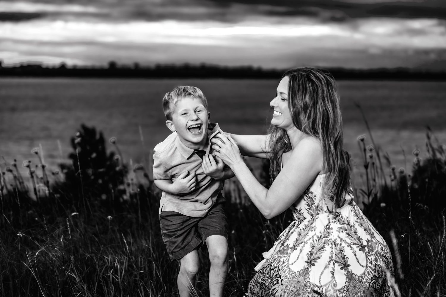 A heartwarming black and white moment captured in a field as laughter fills the air on a cloudy summer day.