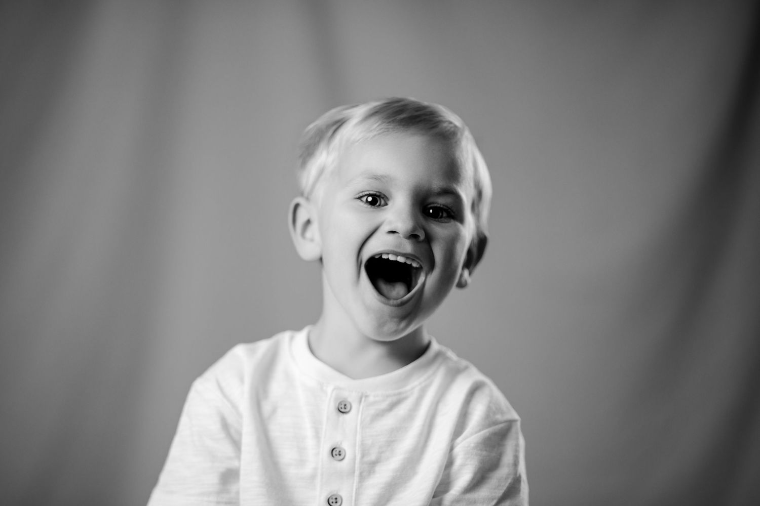 Laughing blond boy in white shirt captured in black and white studio portrait.