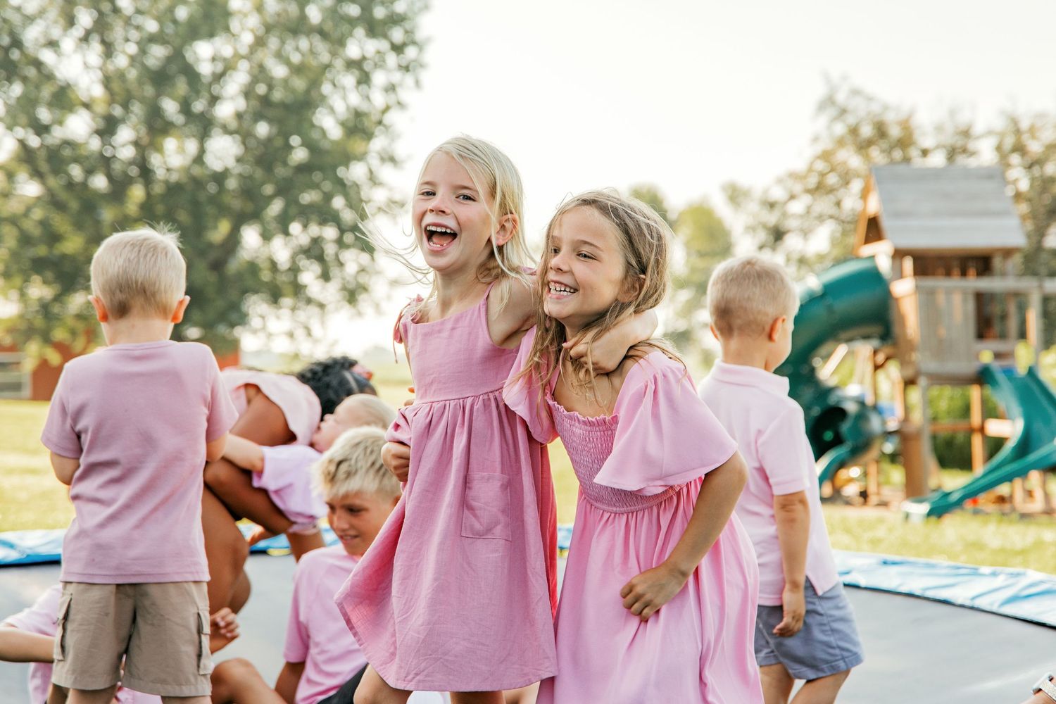 Children playing and laughing together on a playground with pink dresses and casual attire.