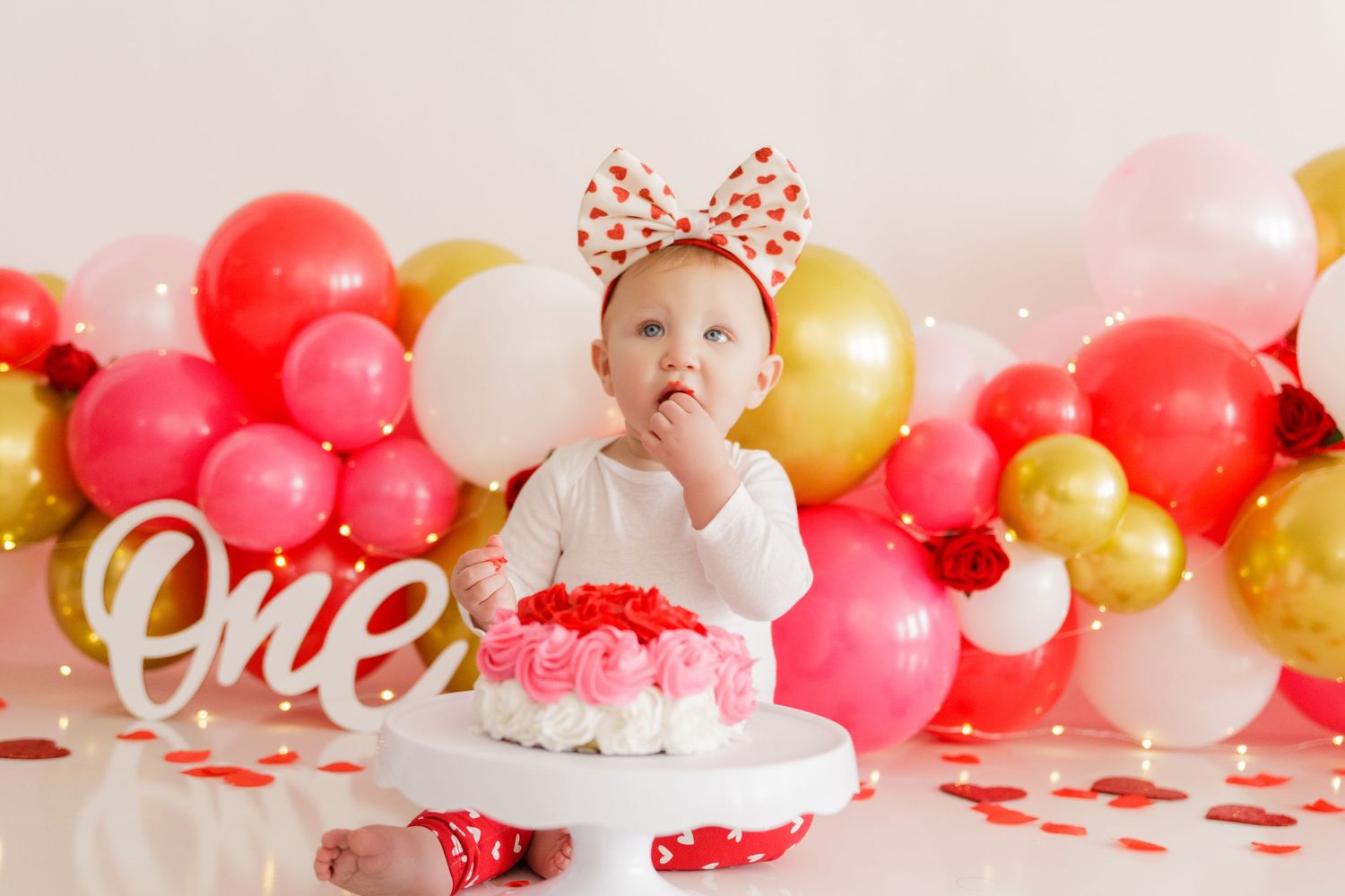 First birthday setup with cake, balloons in pink and gold, and 'one' sign for celebration.