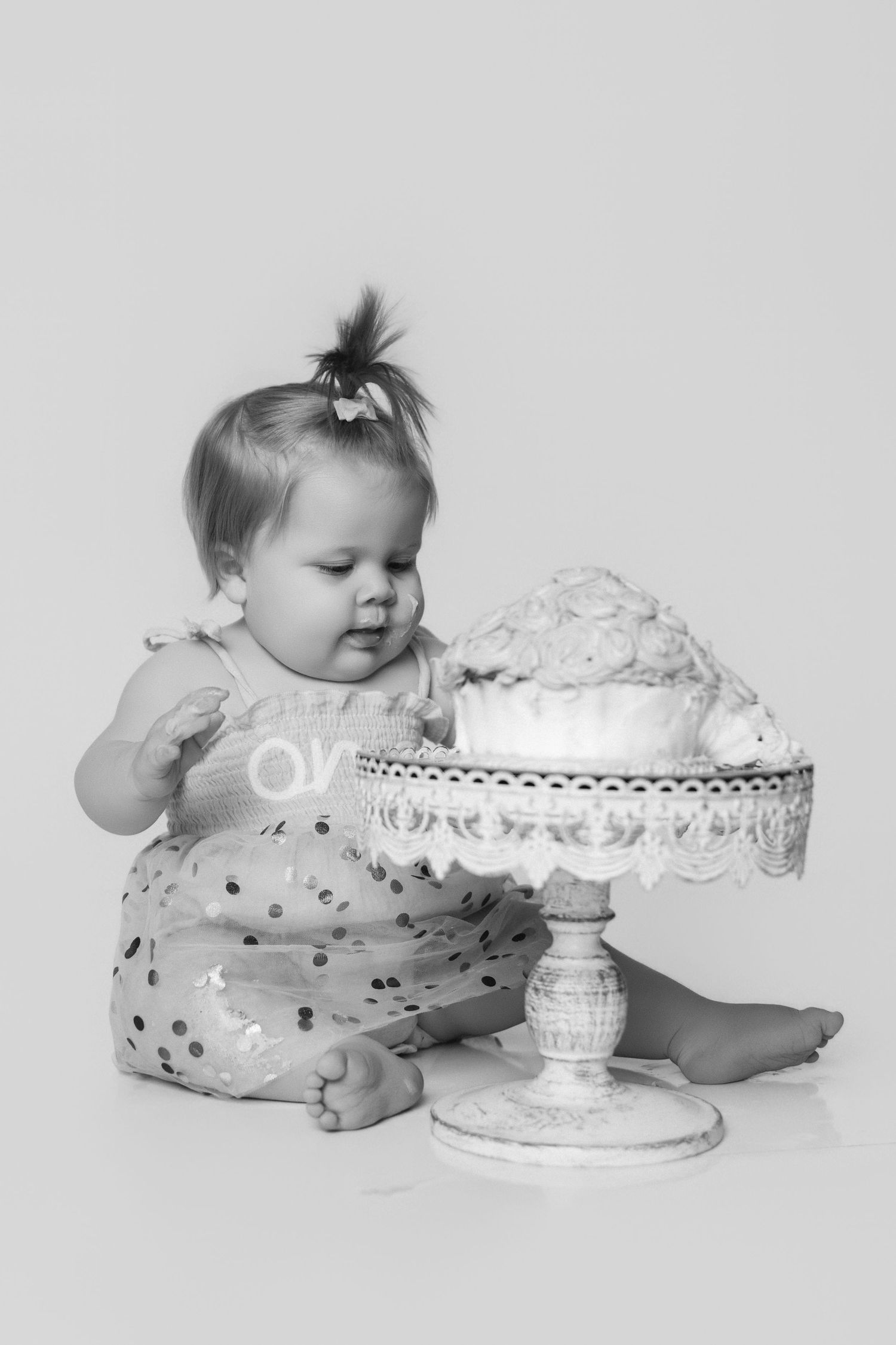 Black and white portrait of baby with elegant cake stand during milestone photoshoot.